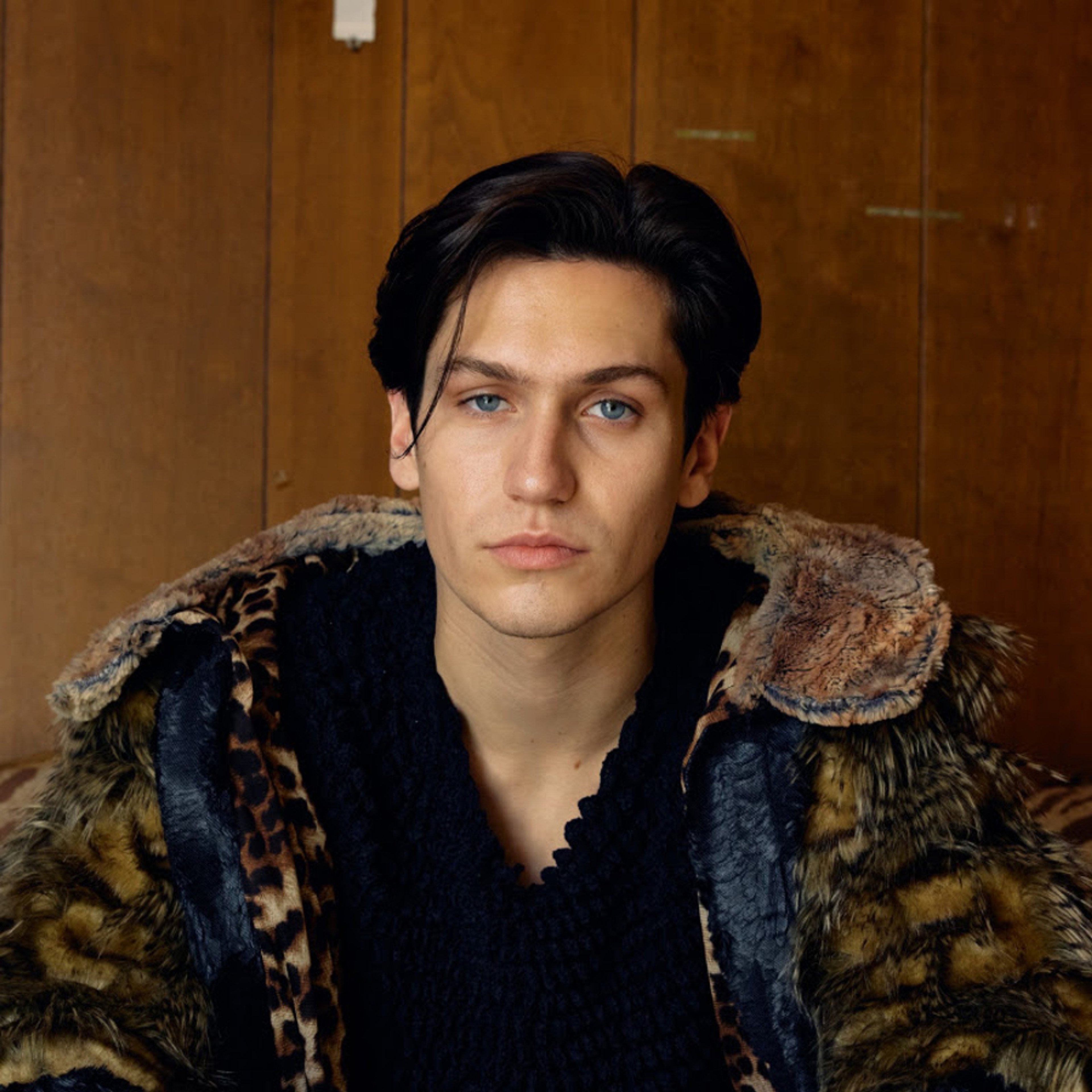 A young man with dark hair wearing a fur-trimmed jacket