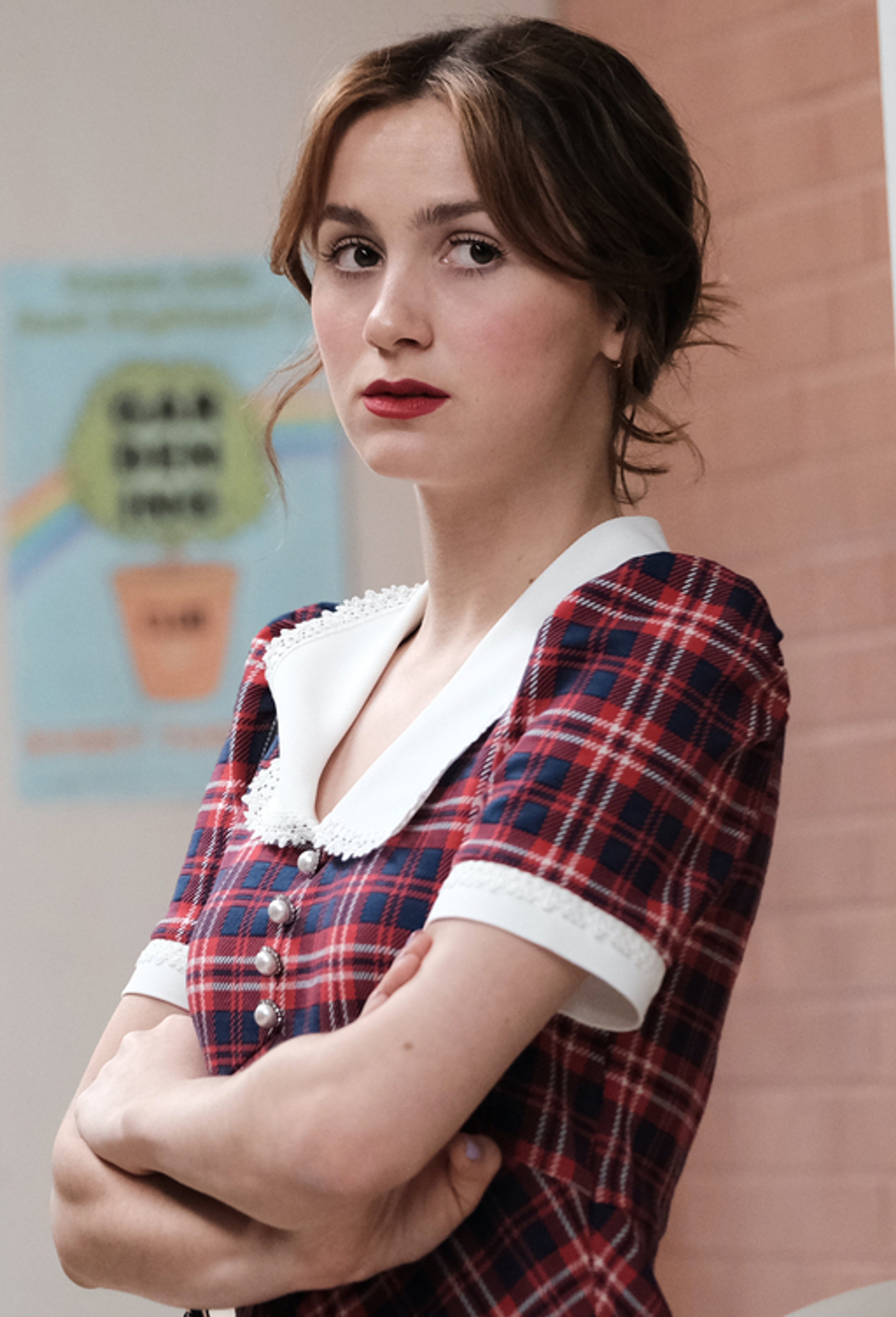 A young woman with dark hair wearing a plaid shirt, looking thoughtful.