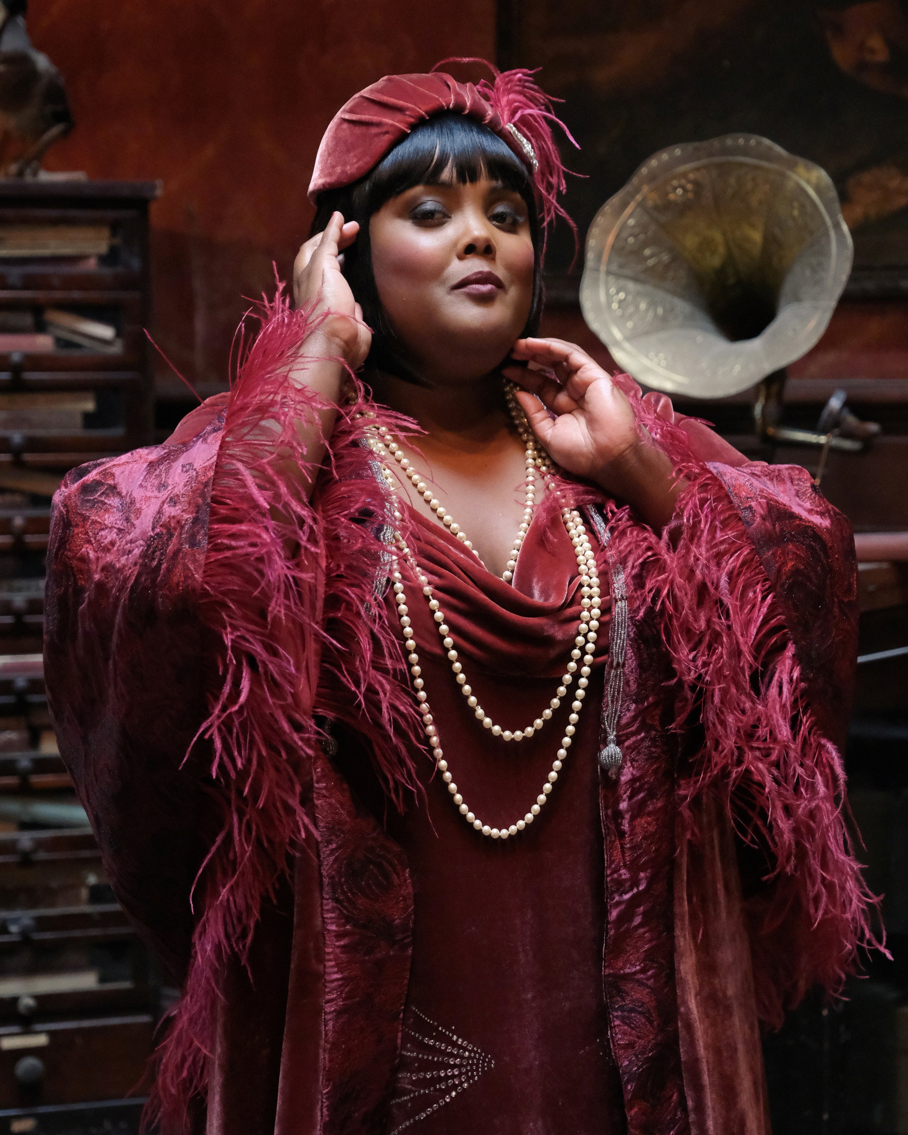 A glamorously dressed 1920s-era Black woman with a confident expression, wearing a red feathered dress and hat.