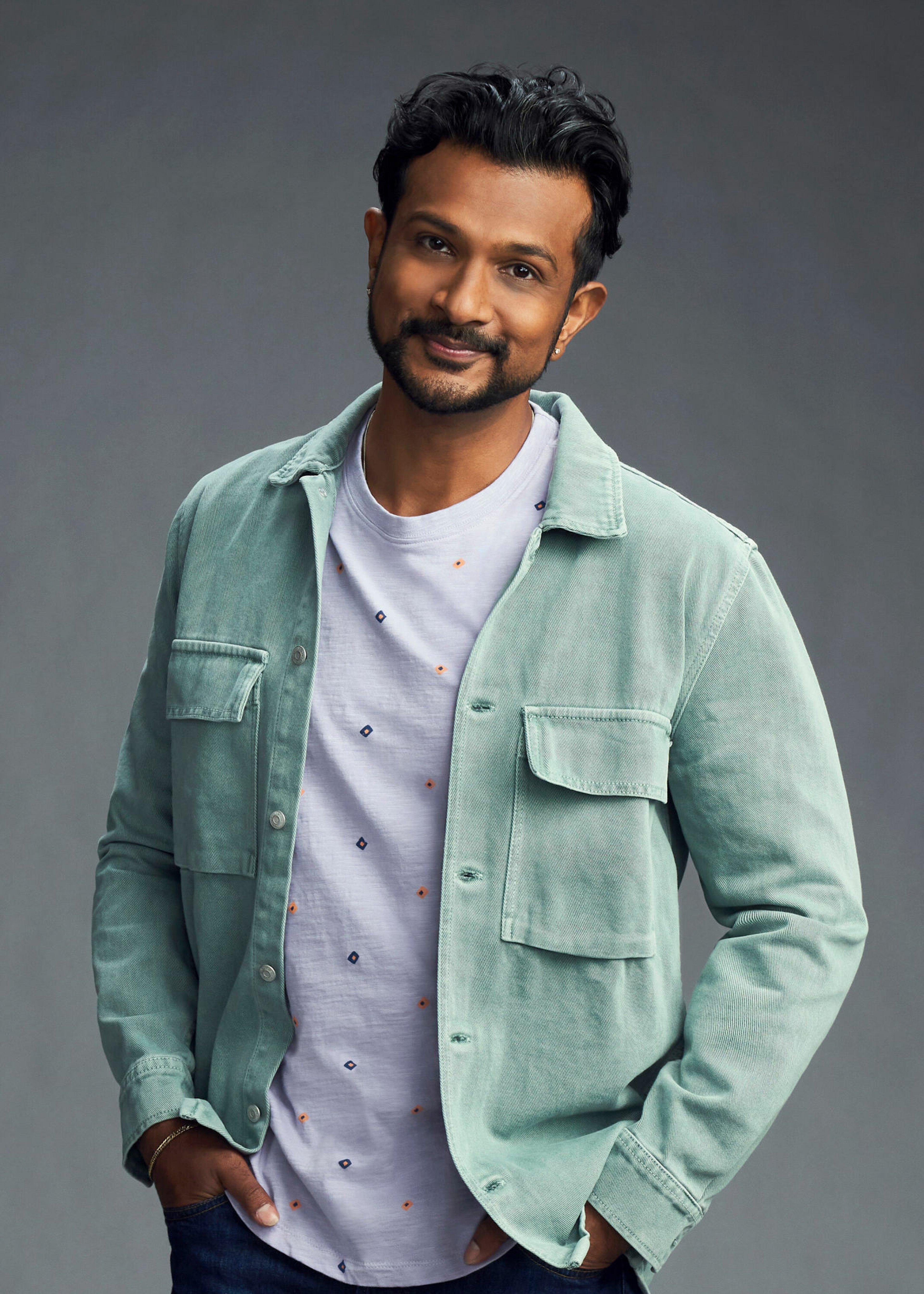 A man with dark hair and a beard wearing a light green jacket, with a friendly expression on his face.