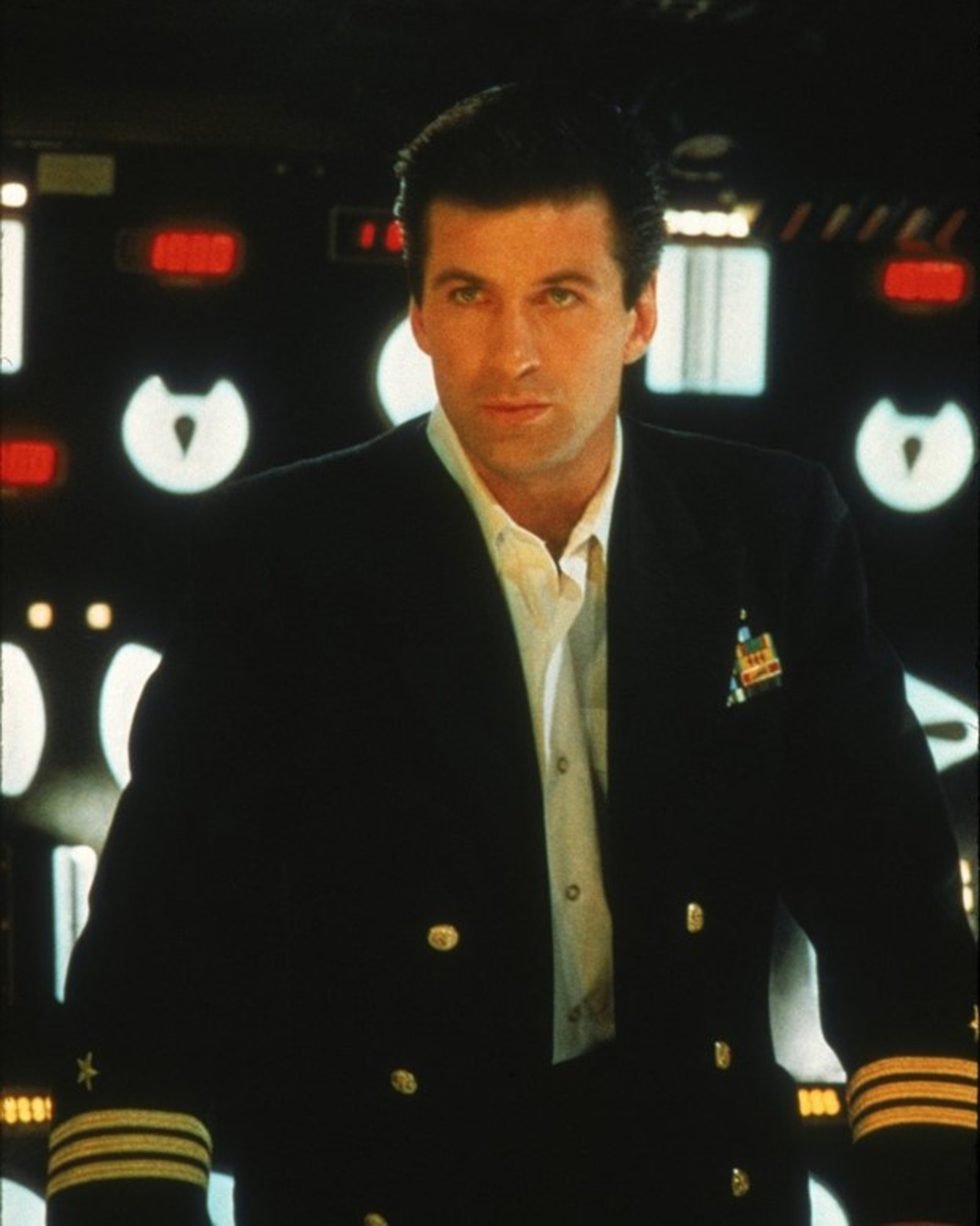 A man in a navy blue uniform with gold epaulets standing in a command center or control room setting