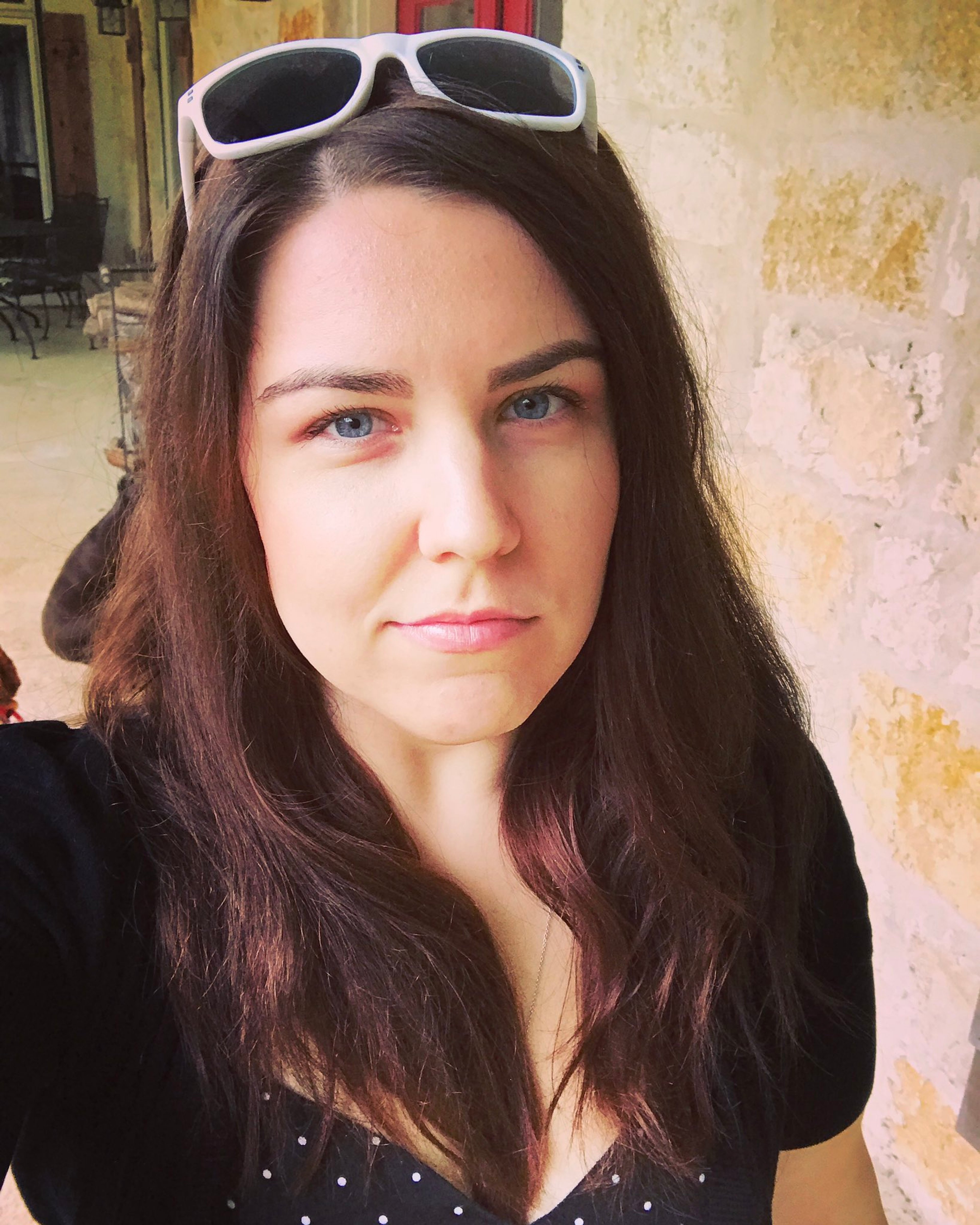 A young woman with long brown hair and sunglasses, smiling at the camera.