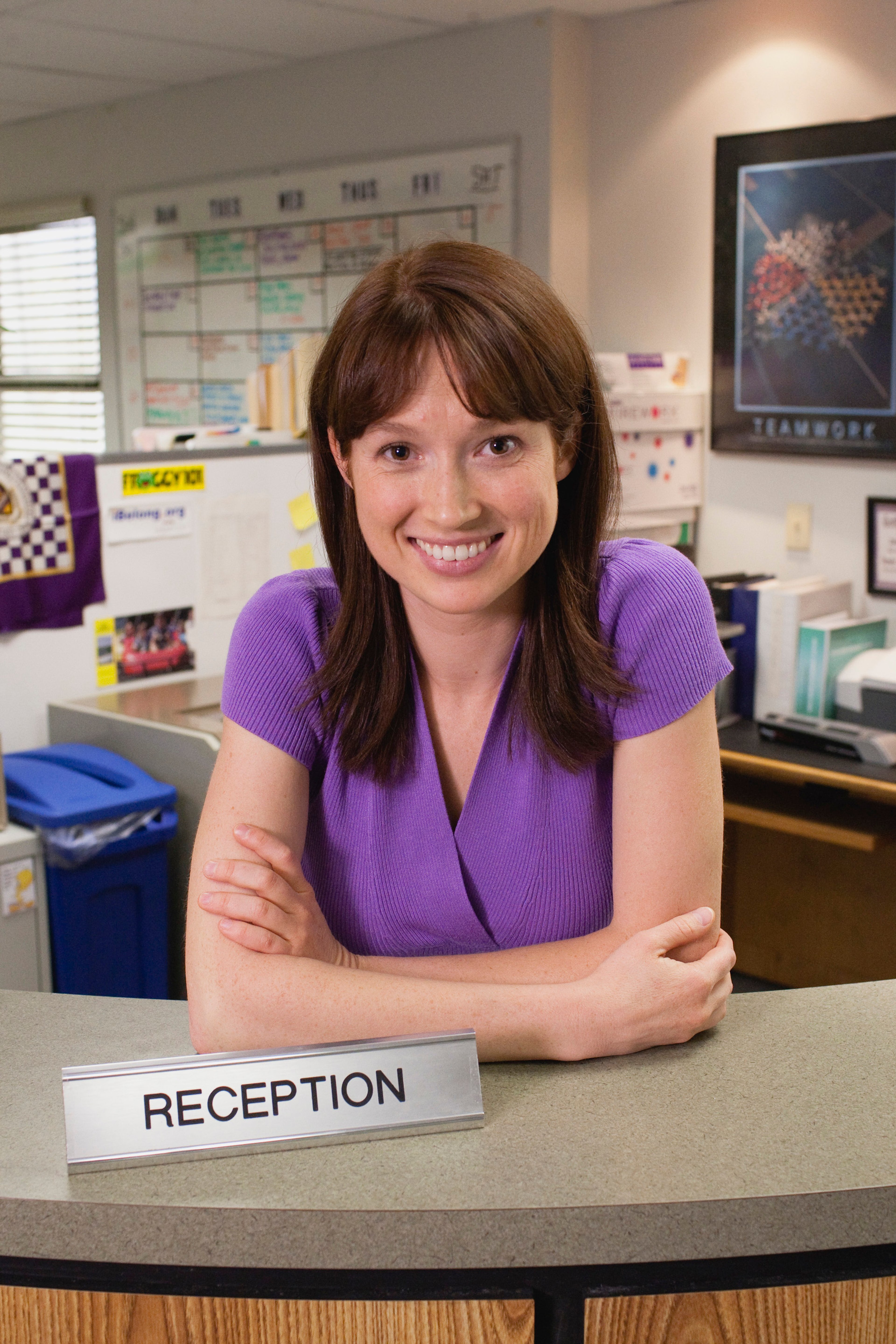 A smiling woman with brown hair sitting at a reception desk