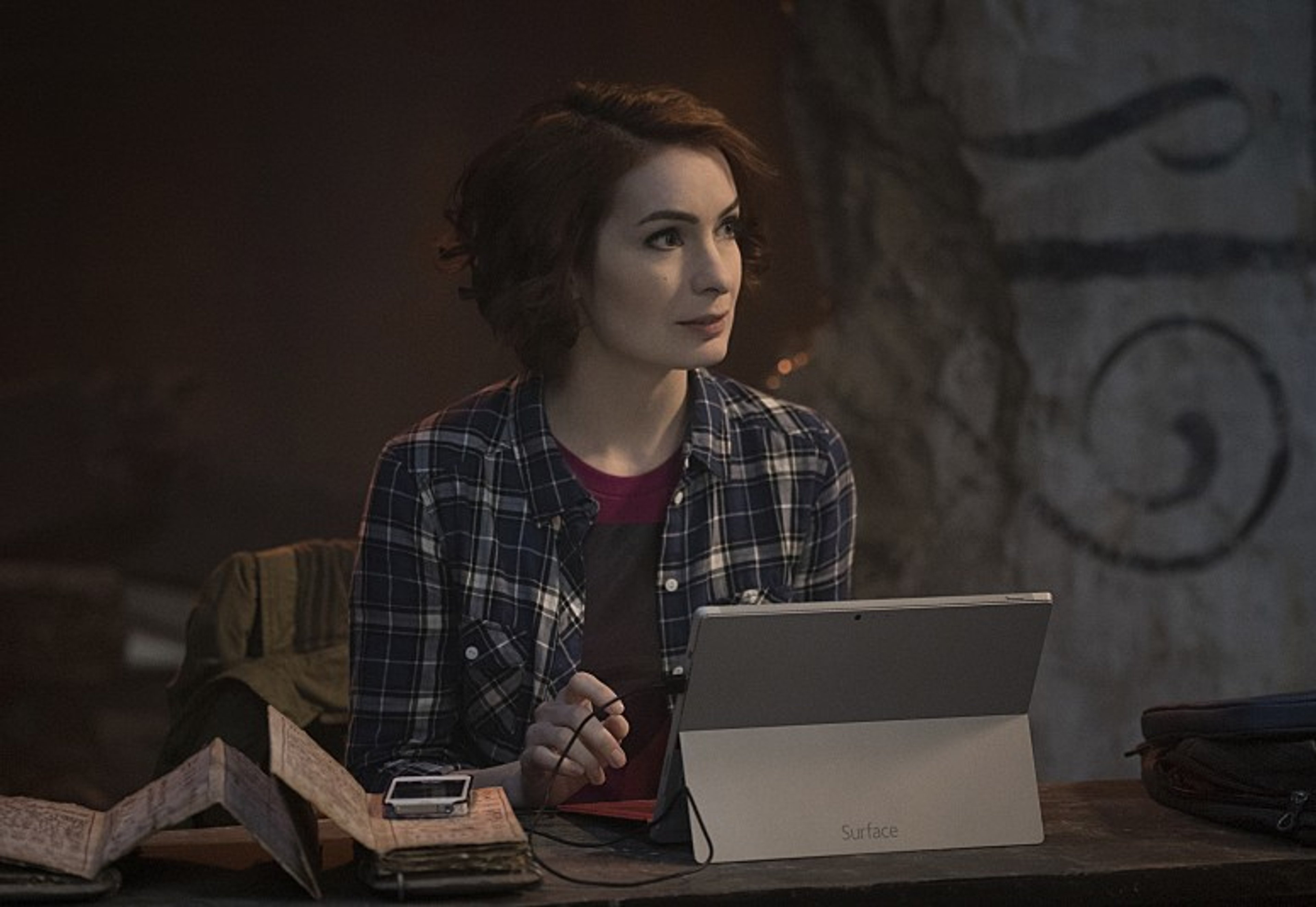 A young woman with curly brown hair sitting at a desk, working on a laptop or tablet.