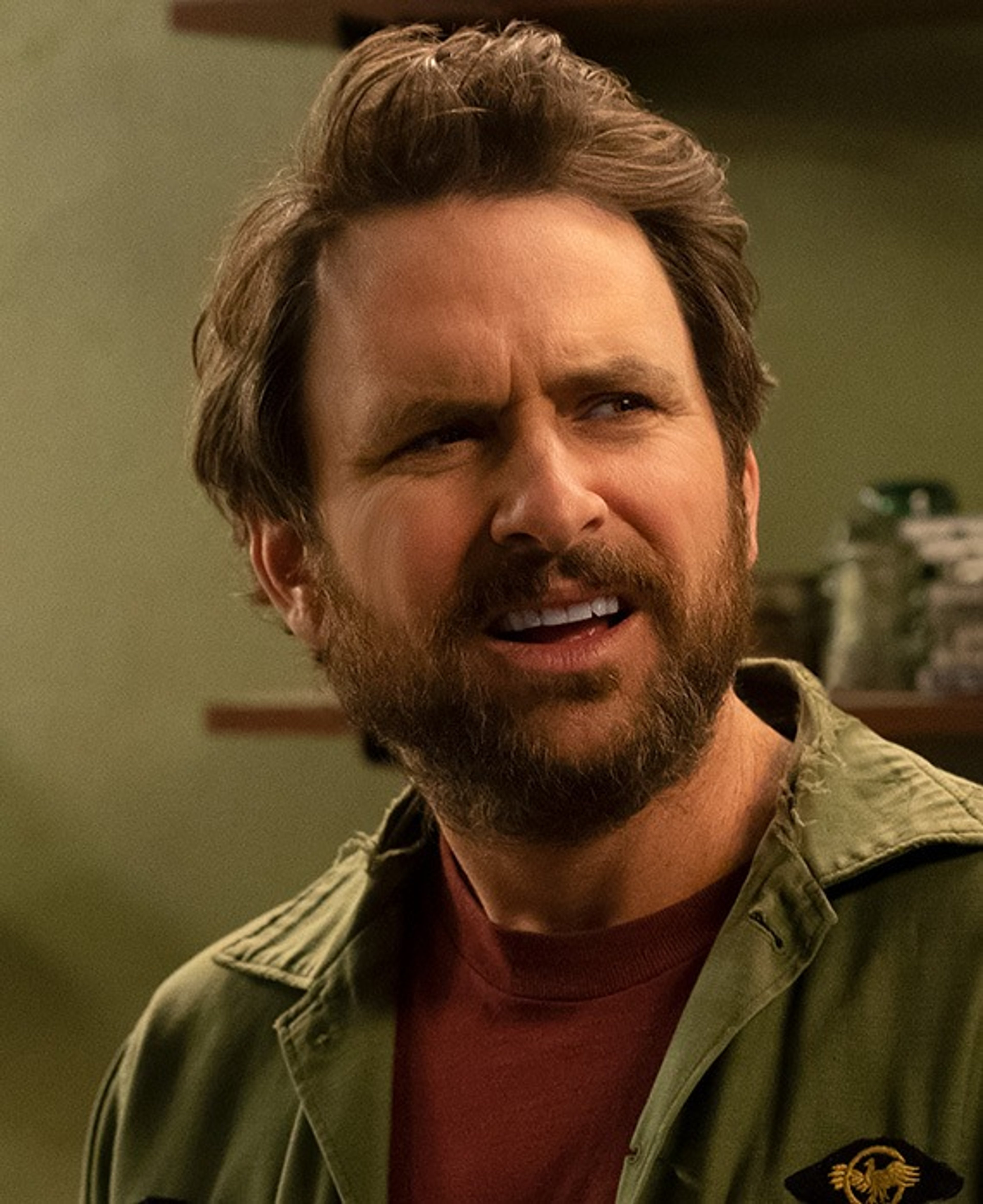 A middle-aged man with a beard and messy hair, wearing a red shirt and green jacket, with an intense expression on his face.