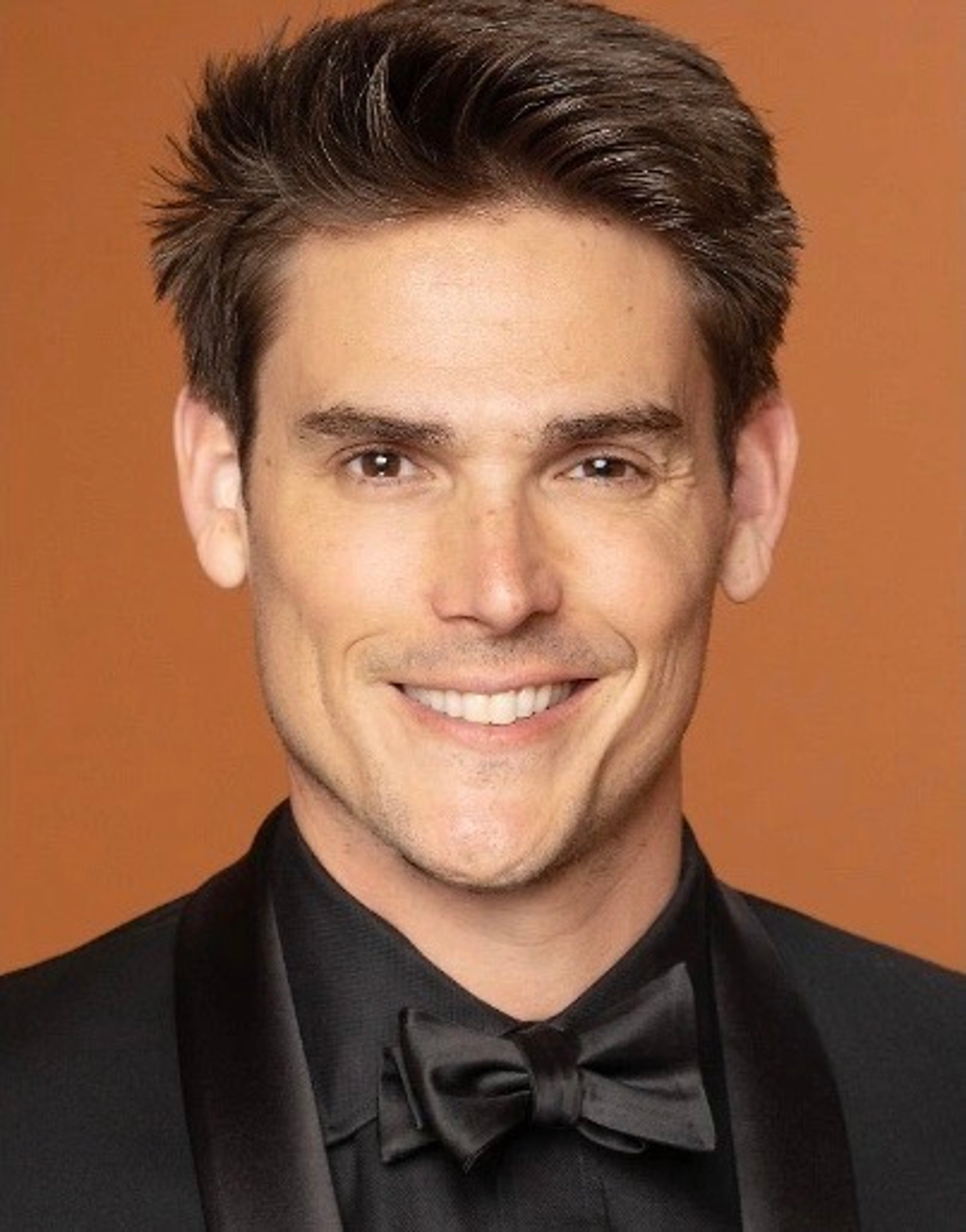 A well-dressed, smiling man in a tuxedo