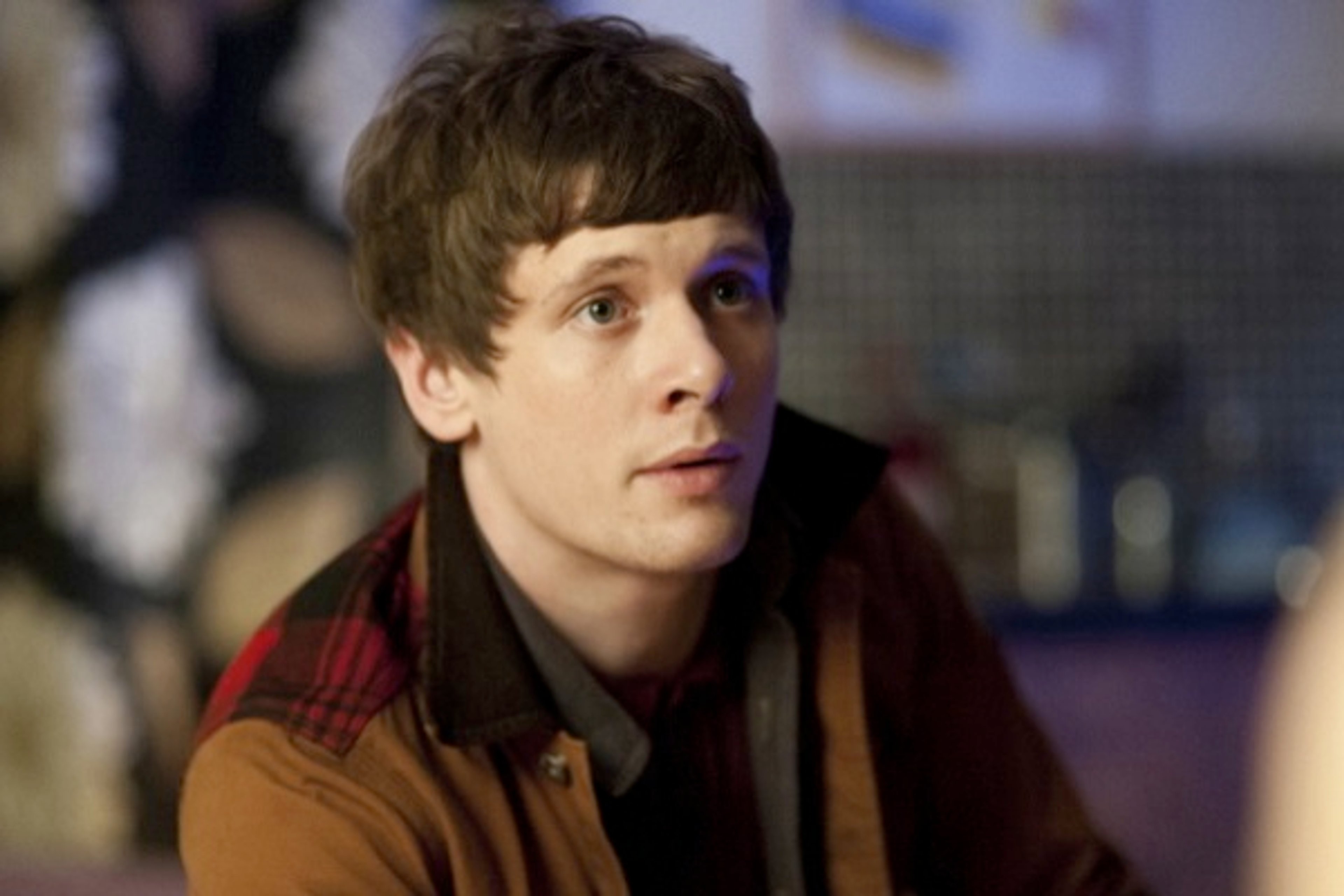 A young man with short brown hair wearing a red and black plaid shirt