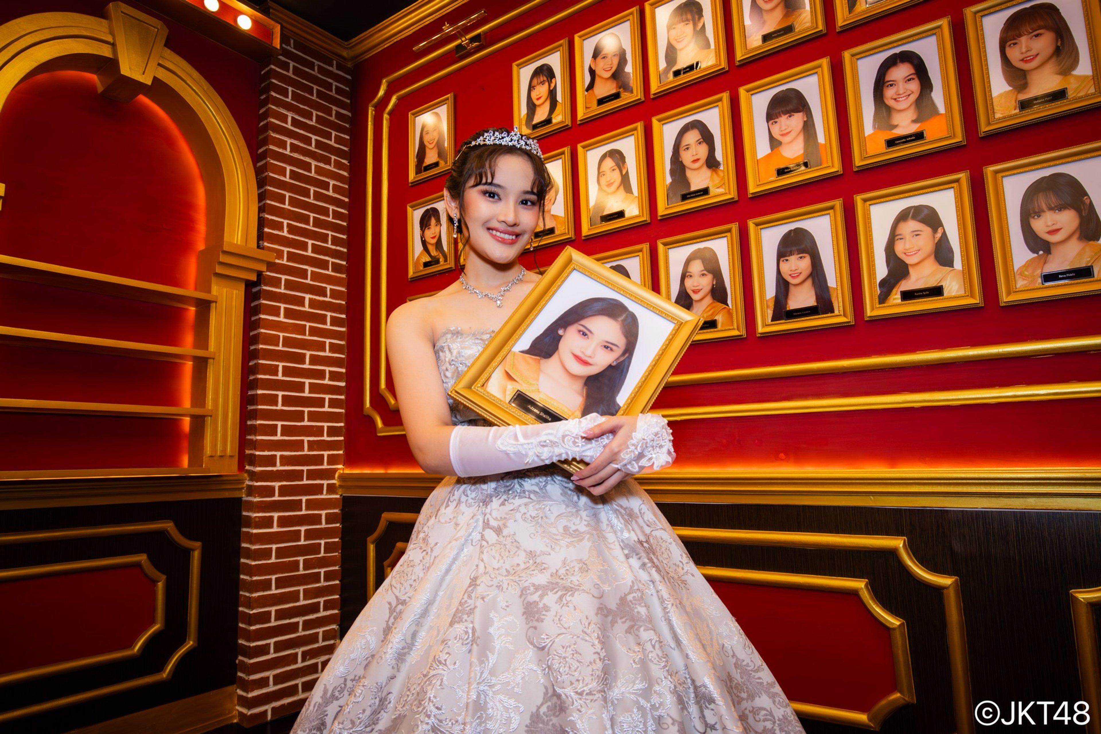 A young woman in a white dress standing in front of a red and gold stage backdrop