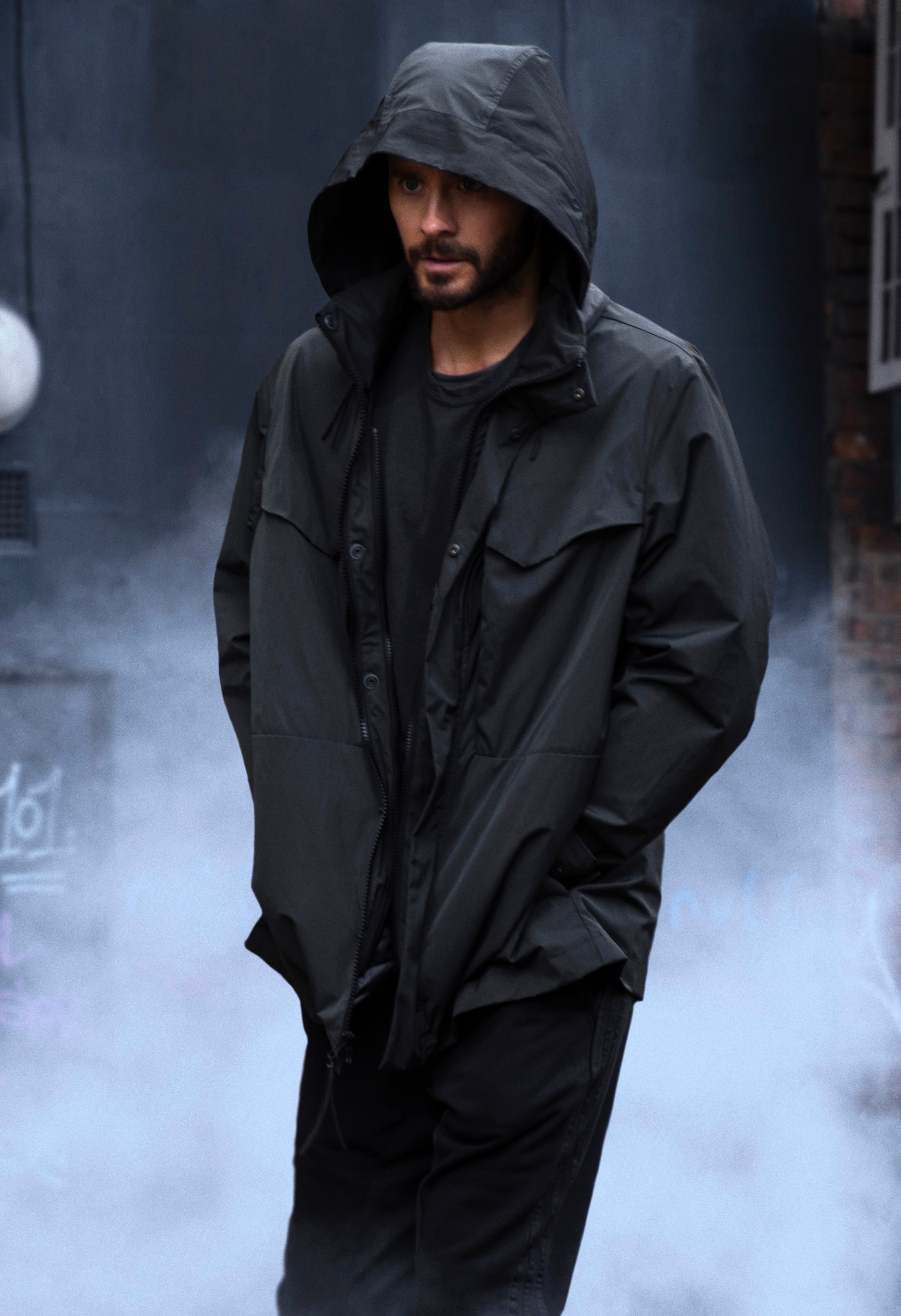 A man in a dark hooded jacket standing in a dimly lit urban setting