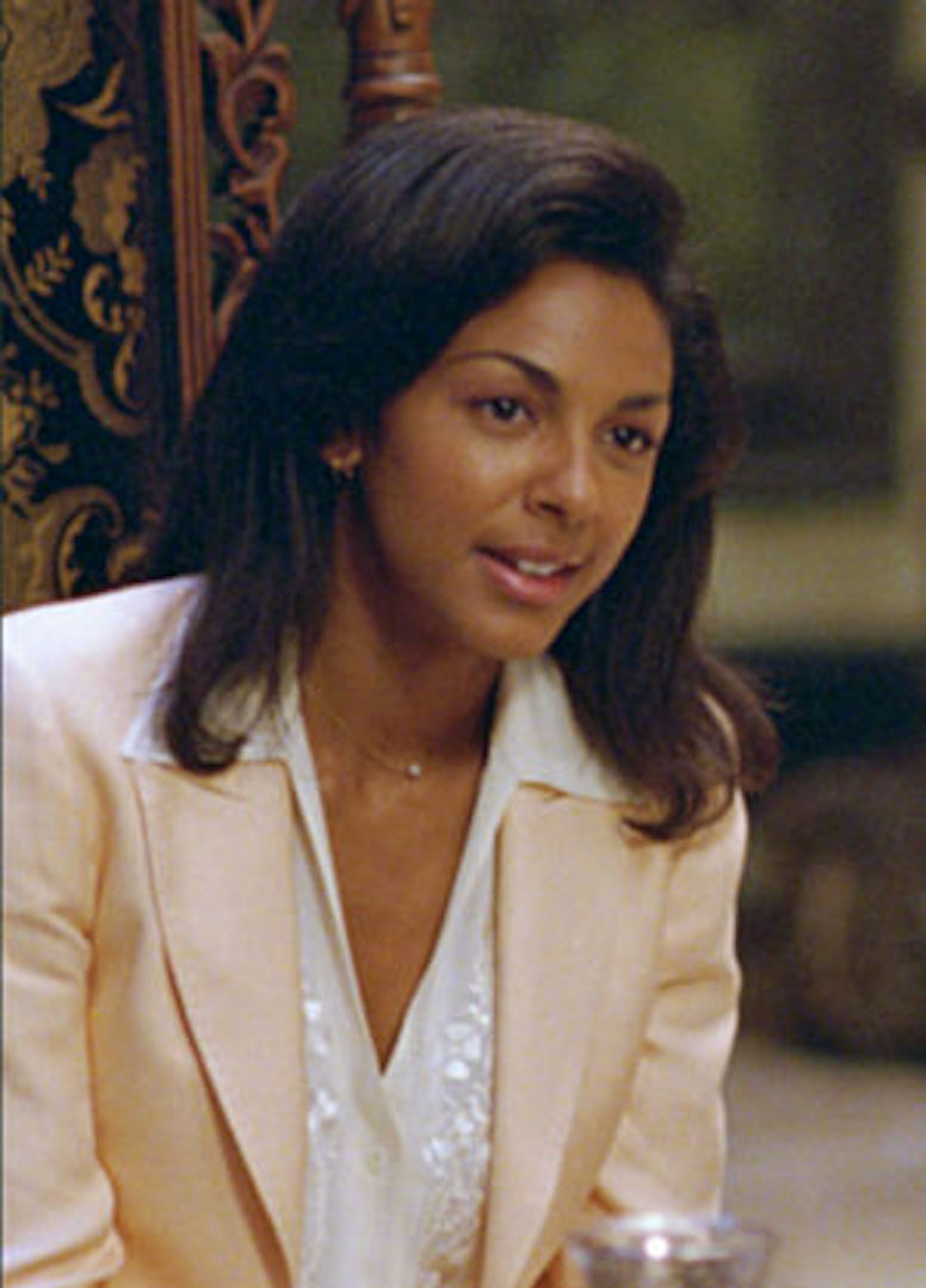 A woman with long dark hair wearing a light-colored blazer, smiling in a professional setting.