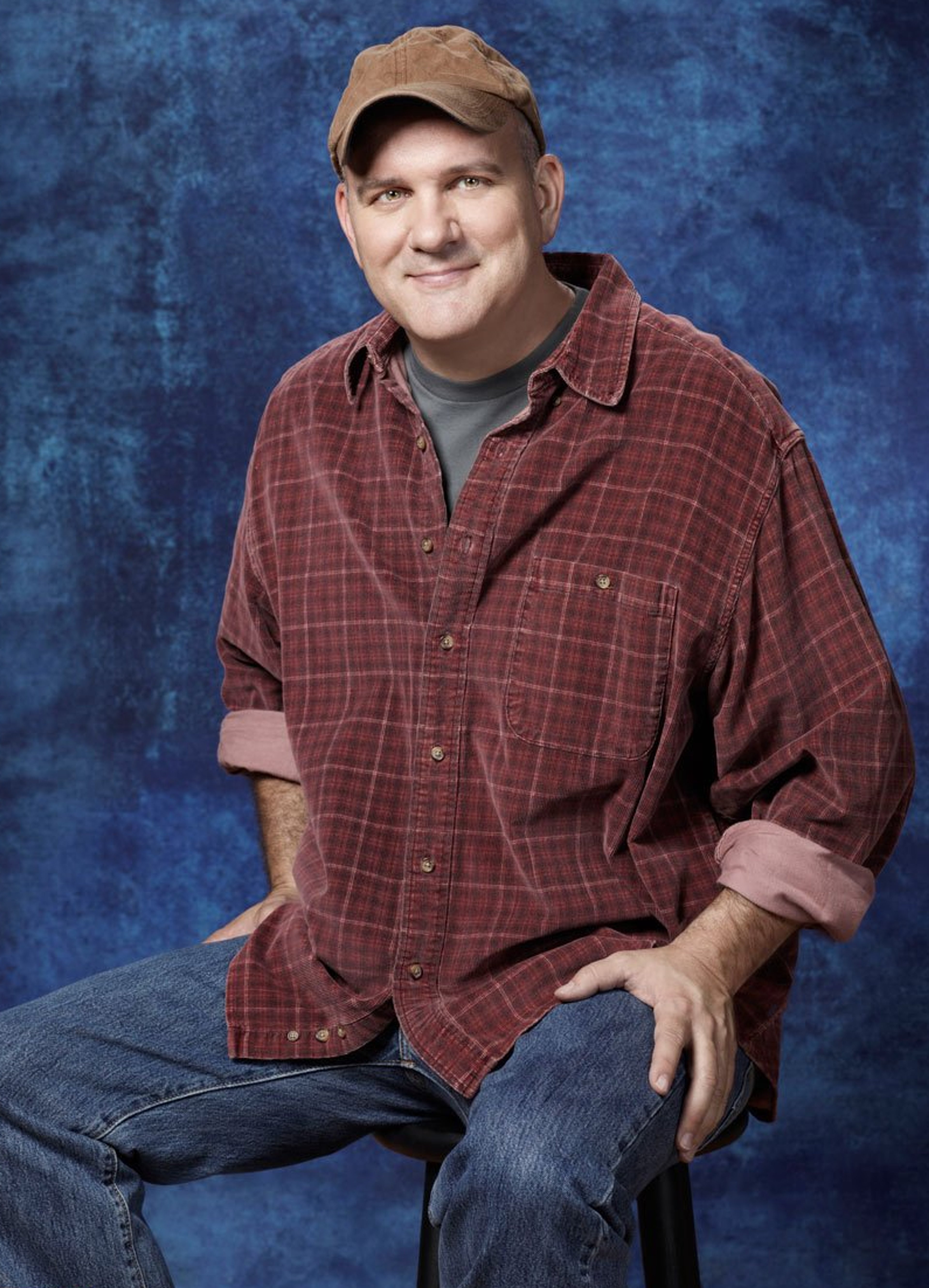 A middle-aged man with a friendly expression wearing a plaid shirt and baseball cap