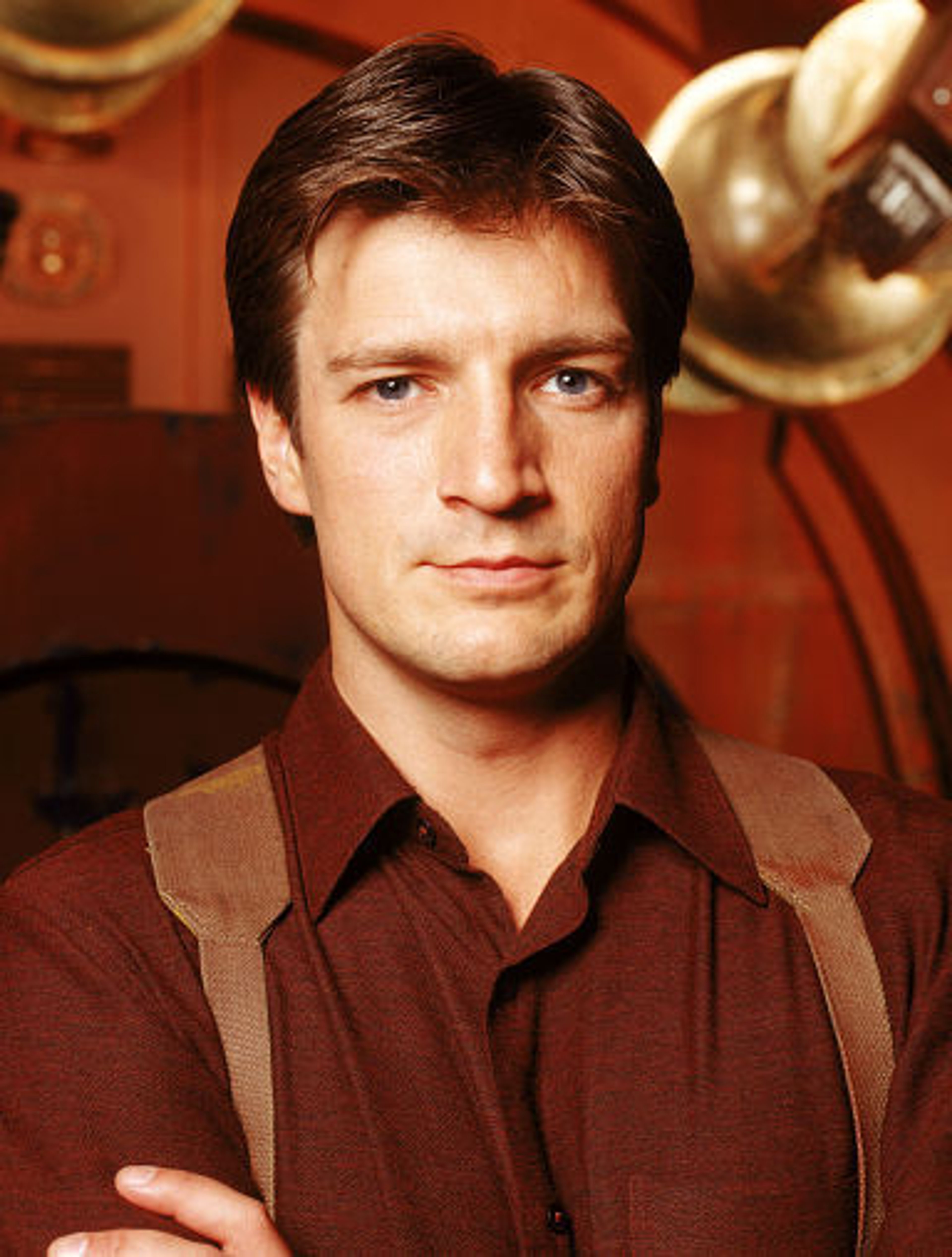 A middle-aged man with short dark hair wearing a brown shirt in a dimly lit setting