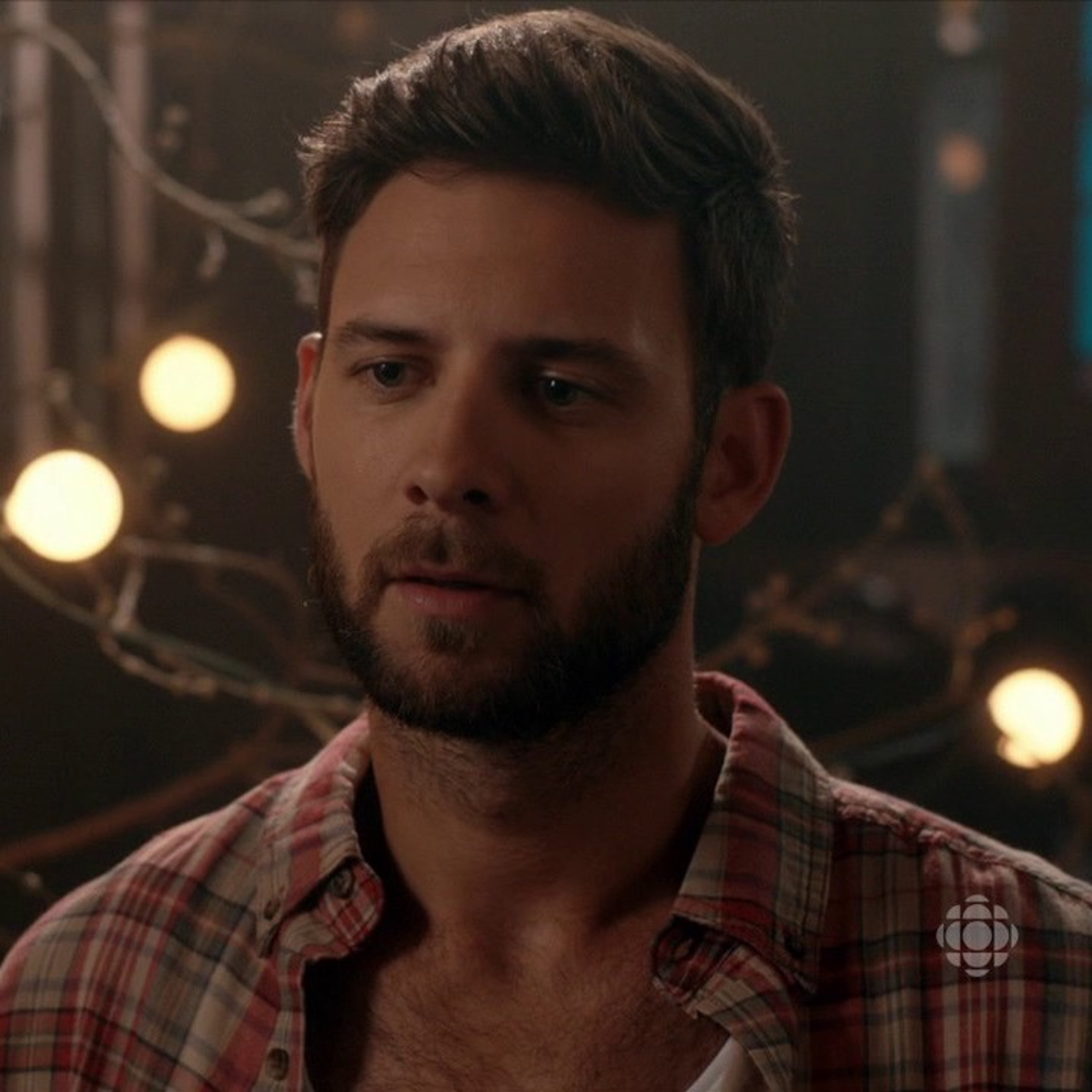 A man with a beard and plaid shirt in a dimly lit setting