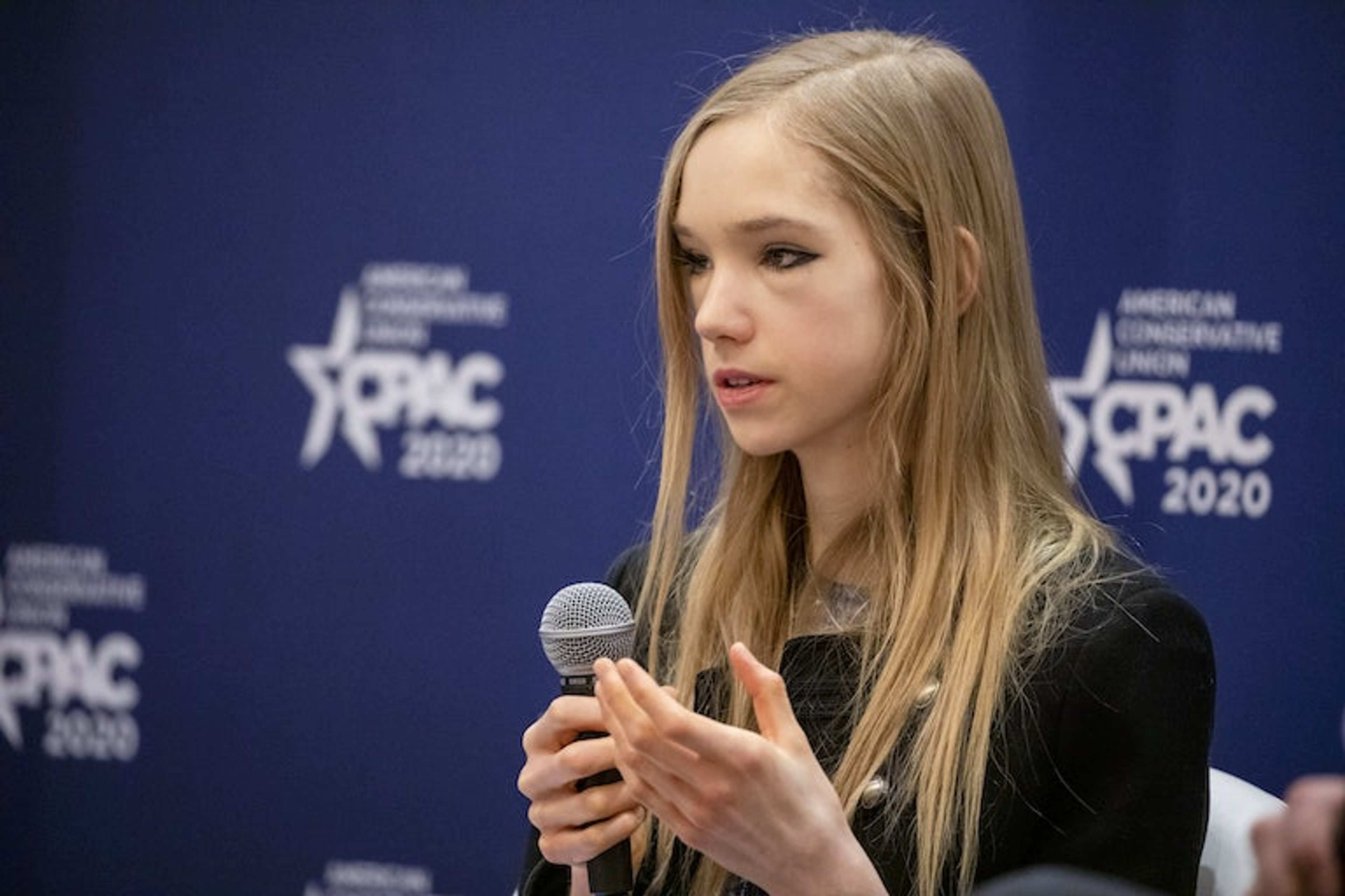A young woman with long blonde hair speaking at a podium