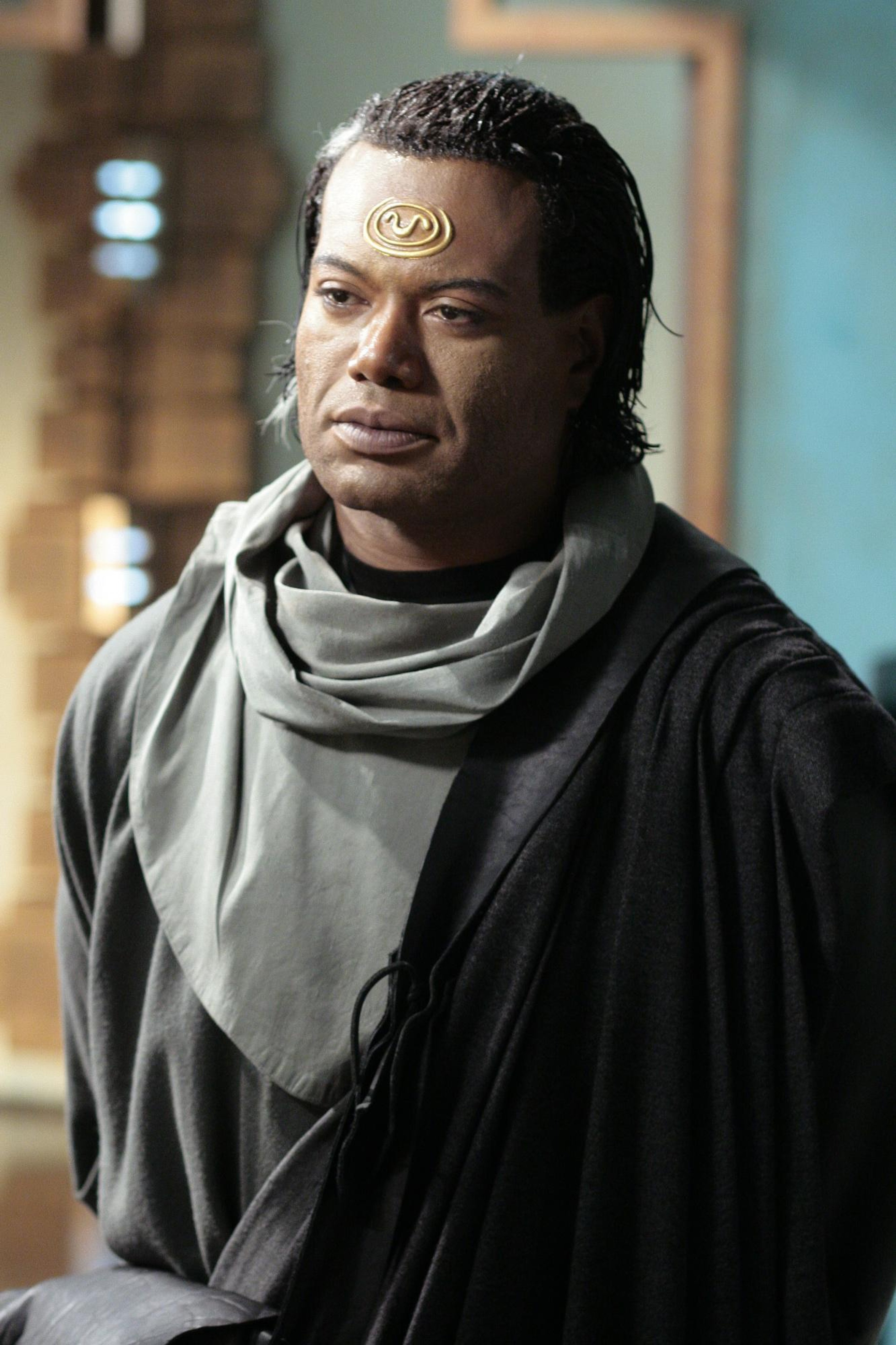 A man with a shaved head wearing a gray robe and scarf