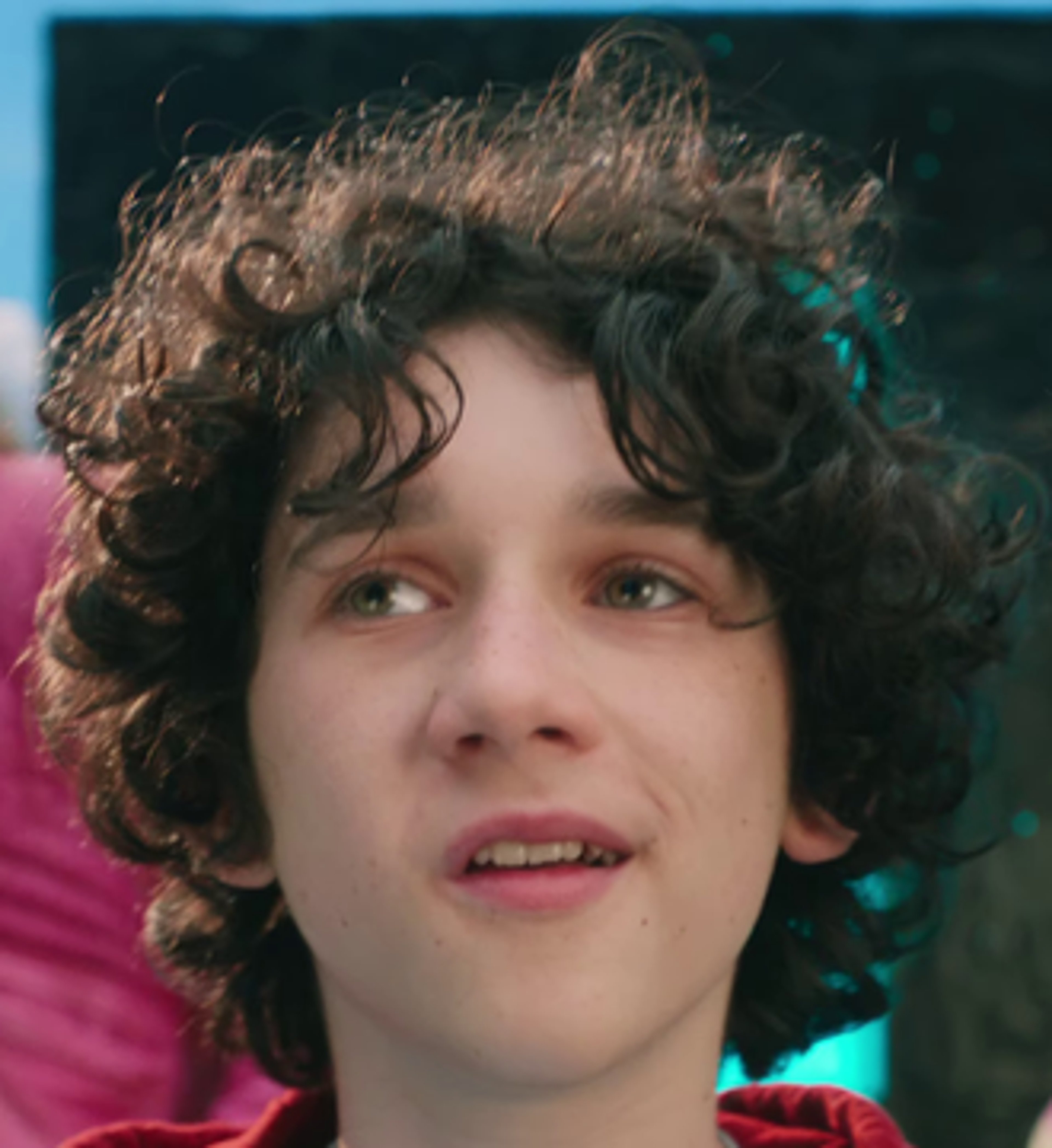 A young man with curly brown hair wearing a red hoodie