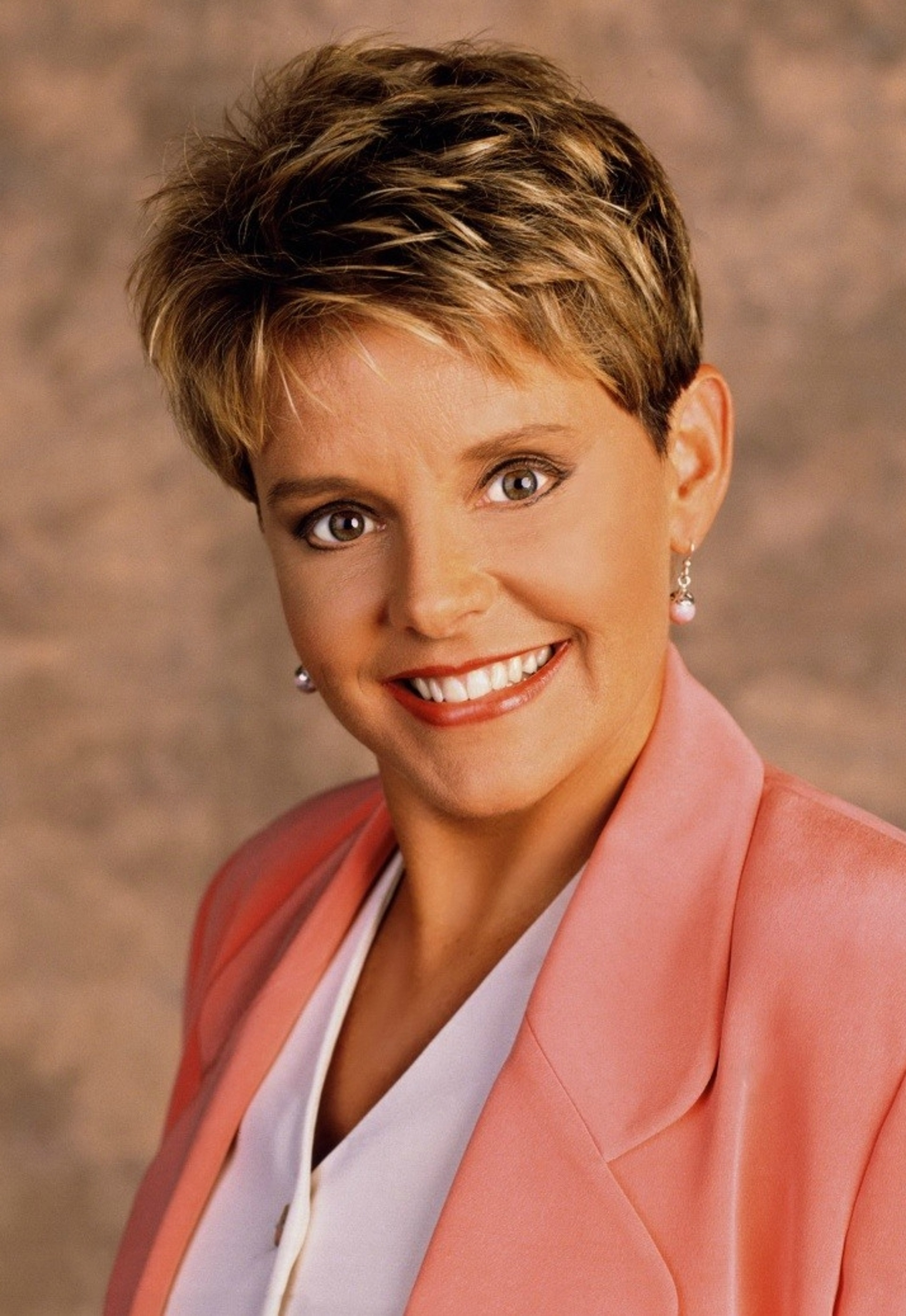 A smiling middle-aged woman with short brown hair wearing a pink blazer