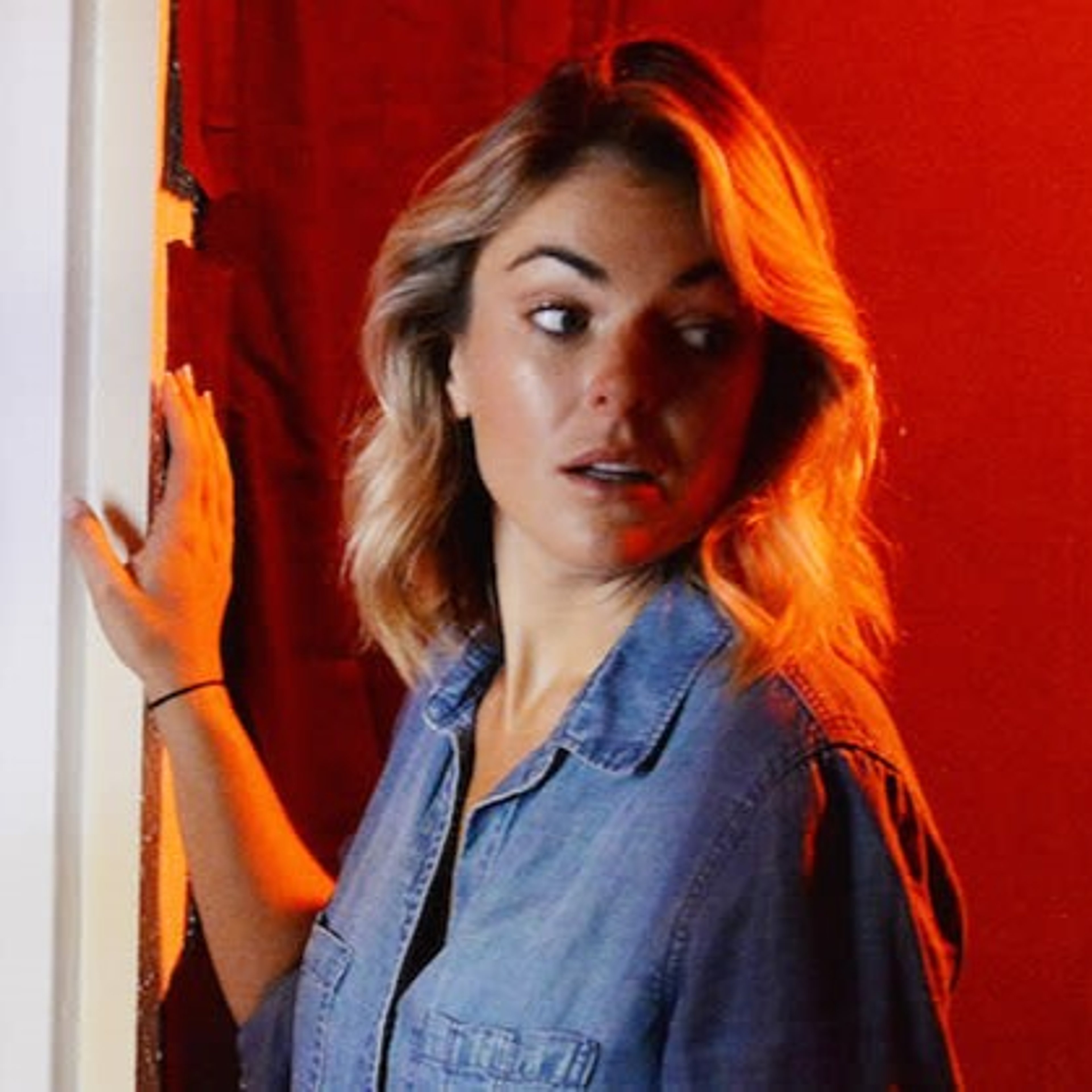 A young woman with blonde hair wearing a denim jacket against a red background