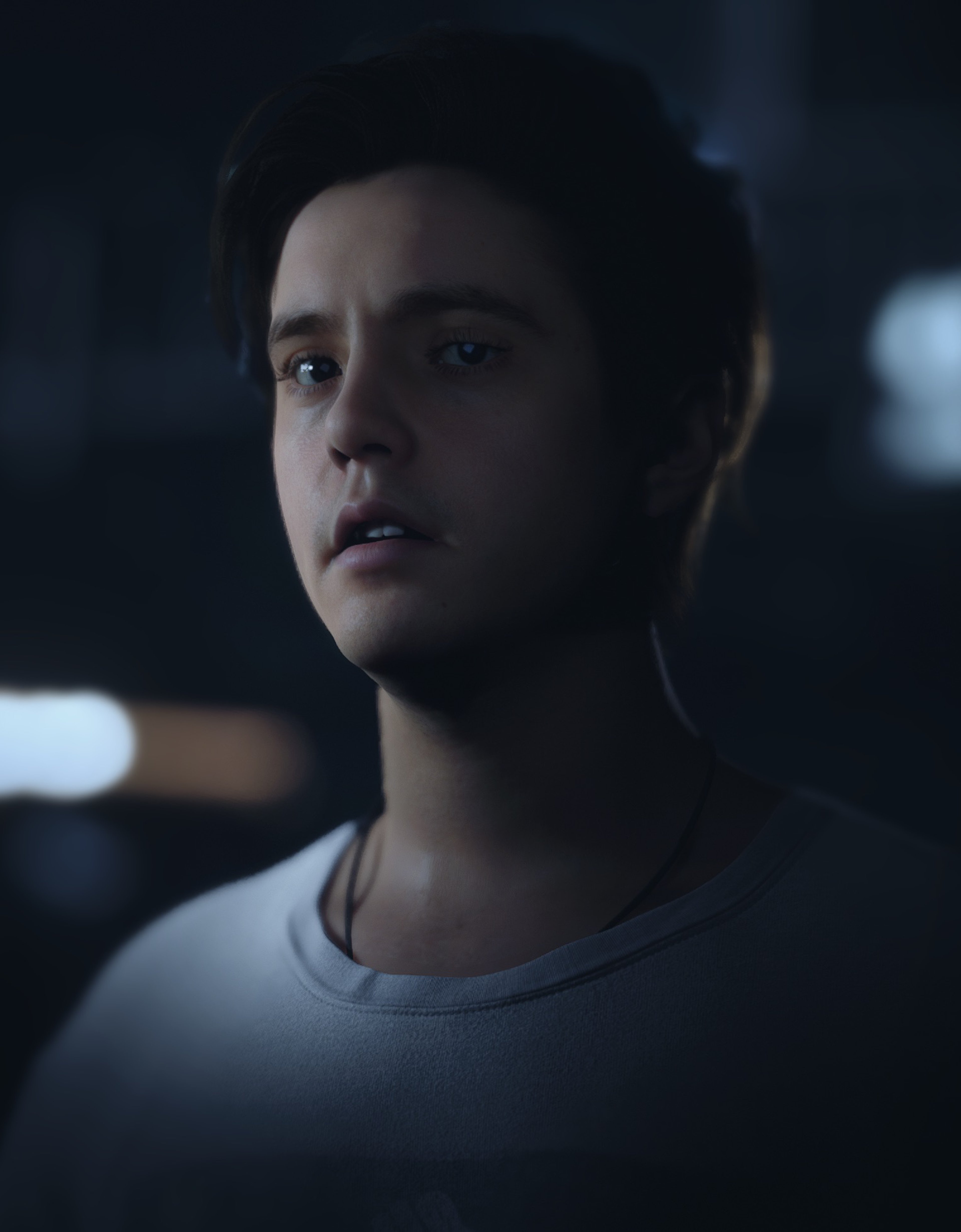 A young man with short brown hair and a wolf tattoo on his arm, looking serious in a dimly lit setting.