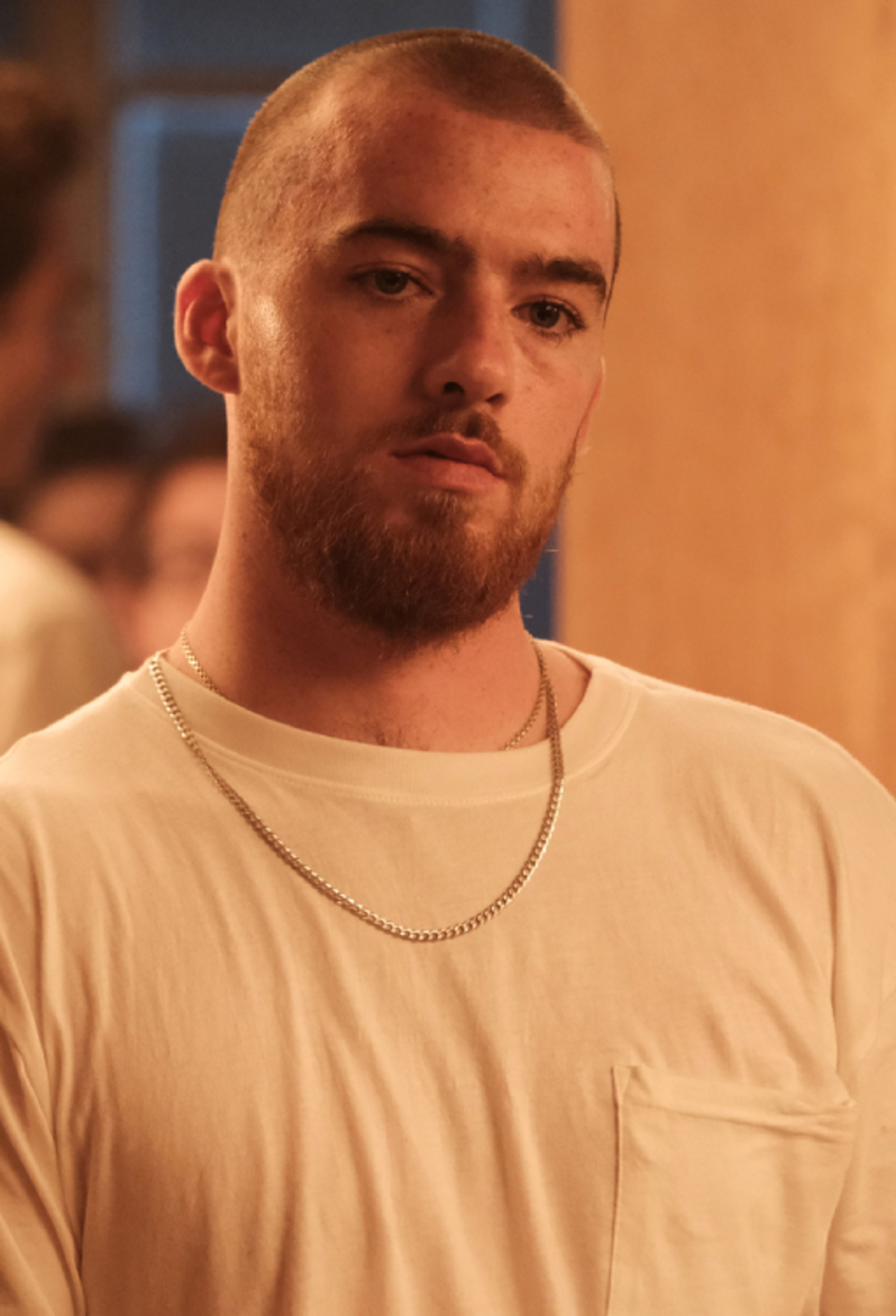 A young man with a shaved head and beard wearing a white t-shirt