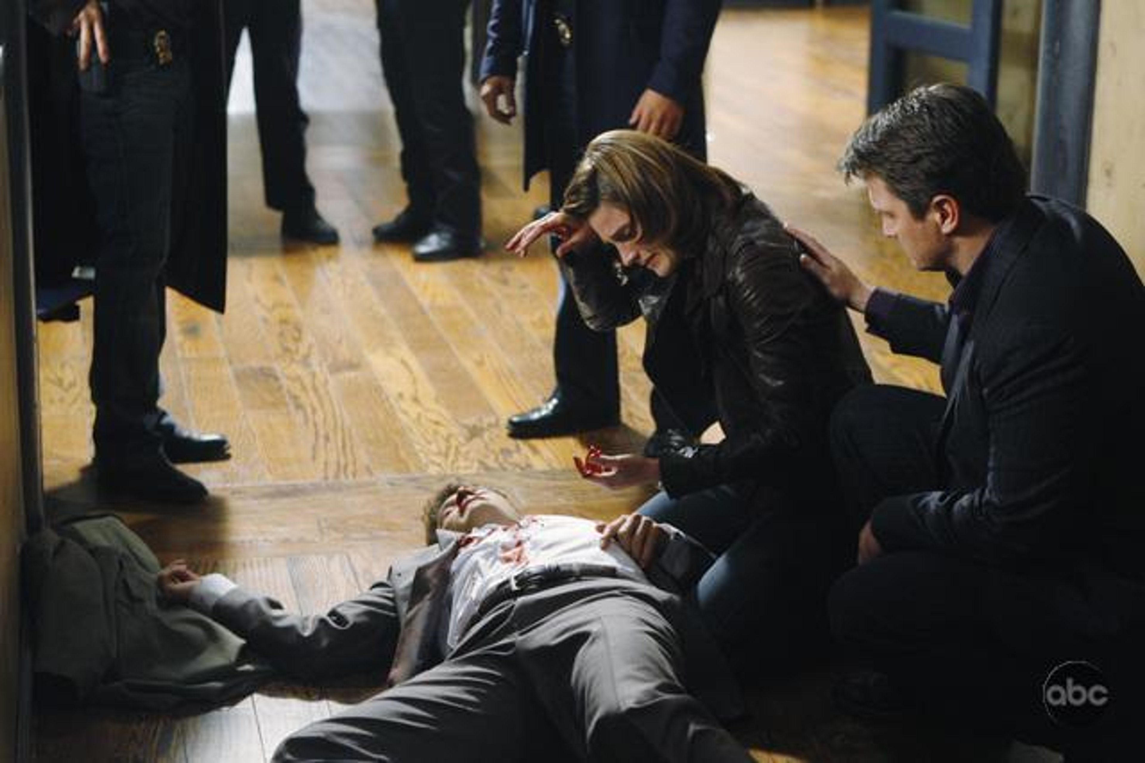 A woman in a dark jacket kneeling next to a man on the ground, with other people in the background.