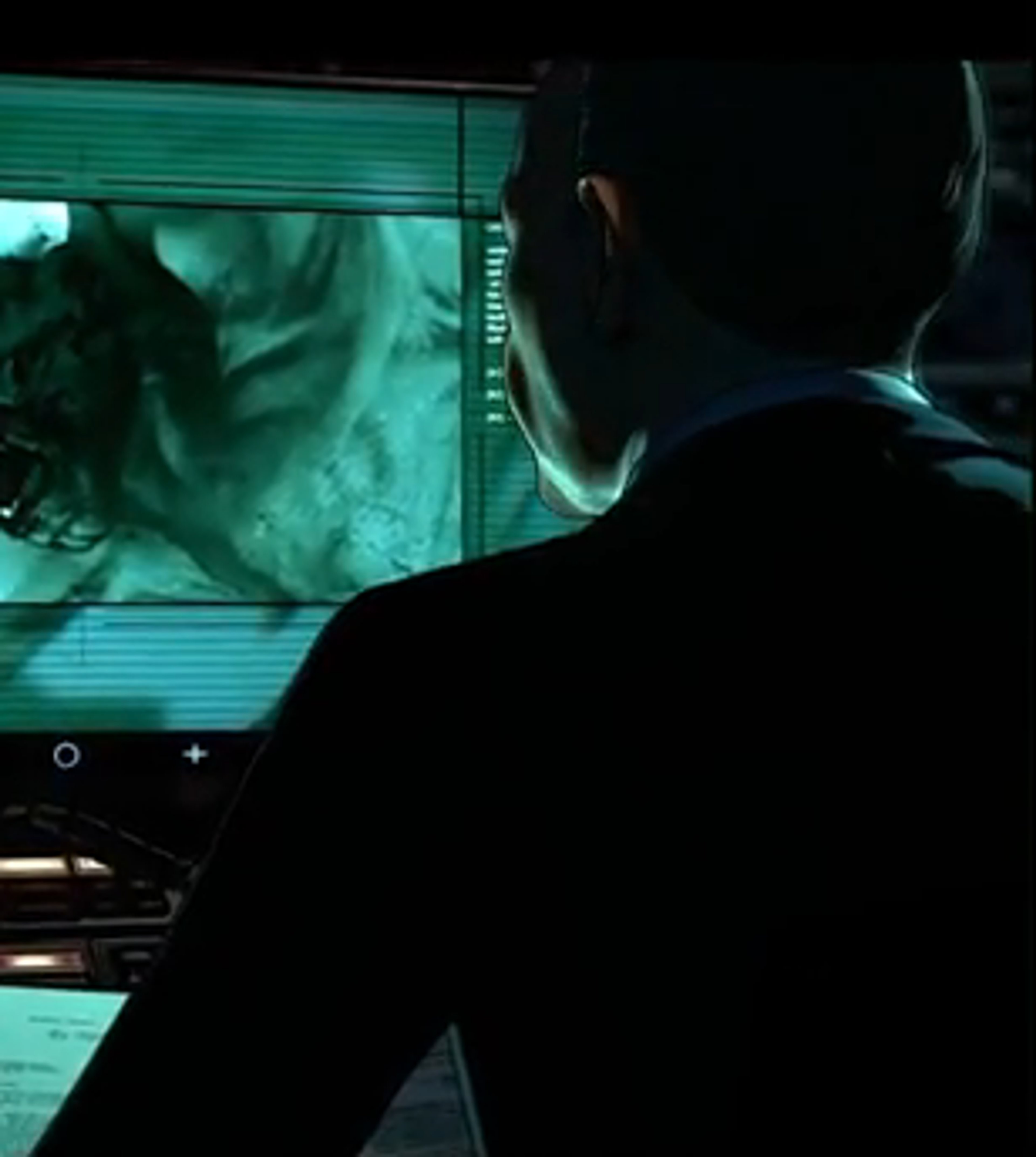 A silhouetted figure sitting in front of a computer screen displaying a green-tinted image.