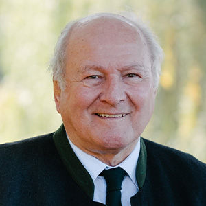 Headshot of Claus Hipp, a middle-aged man in a suit. In the background you can see blurred trees.