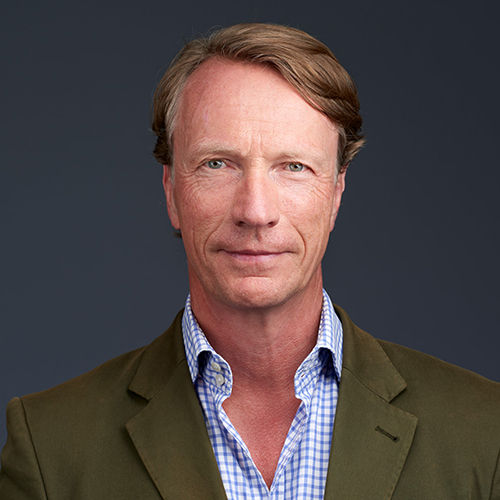 Headshot of Hendrik Brandis, a midle-aged man in a suit on a simple dark gray background.