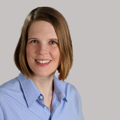 Headshot of Claudia Ferringo, a middle aged woman smiling at the camera on a simple light gray background.