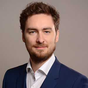 Headshot of Prof. Dr. Philipp Lergetporer, a young man smiling on a simple grey background.