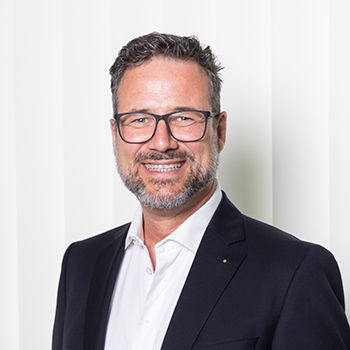 Headshot of Prof. Dr Christoph Ann, a middle aged man smiling on a simple gray background.