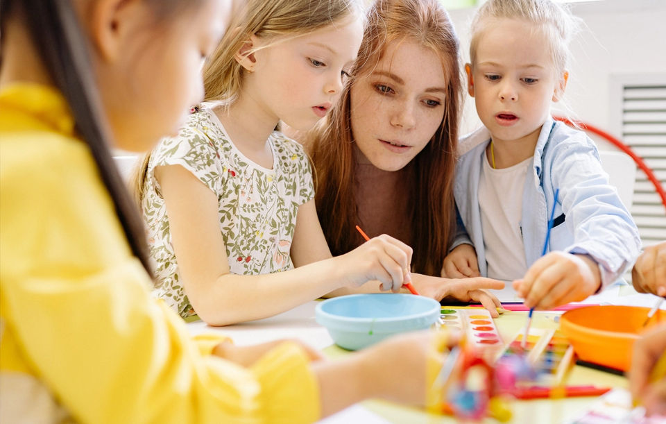 Three students and an adult collaborating on a painting activity in an interactive classroom.