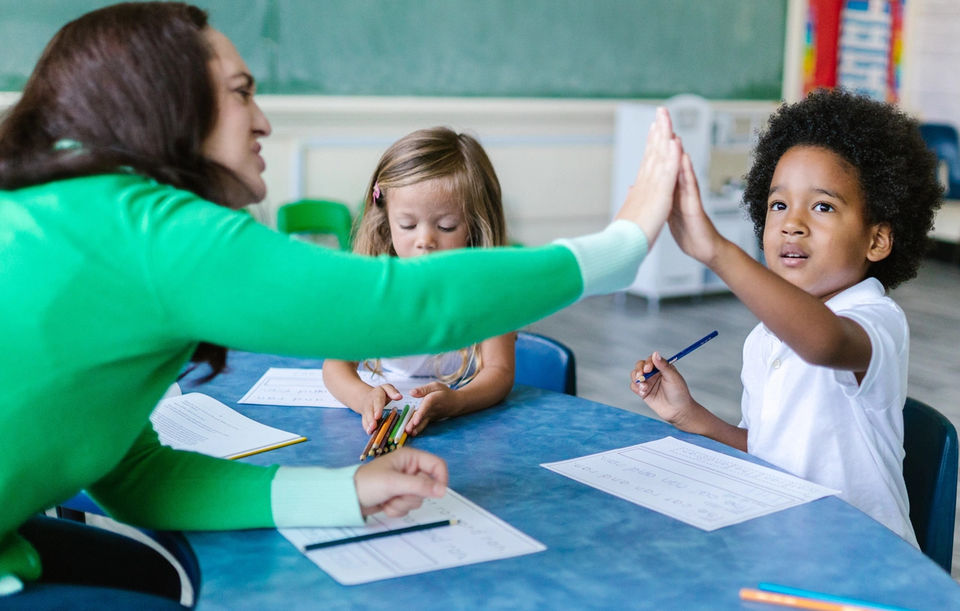 Teacher giving a high five to a student during an activity in an interactive classroom.