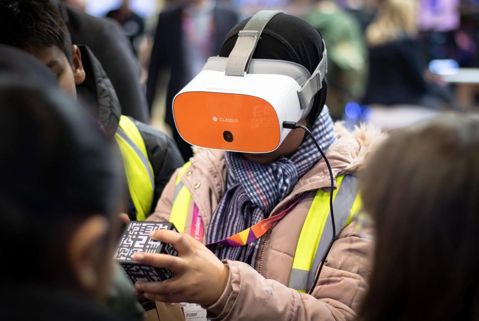 Student wearing a VR headset holding an AR cube as classmates look on