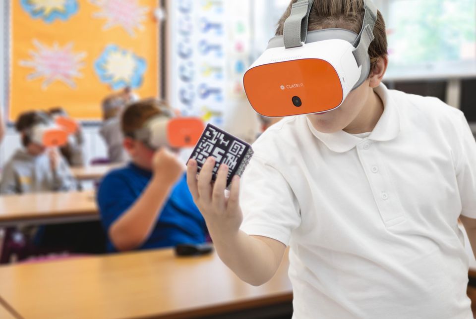 Student wearing a VR headset using an AR cube among fellow classmates