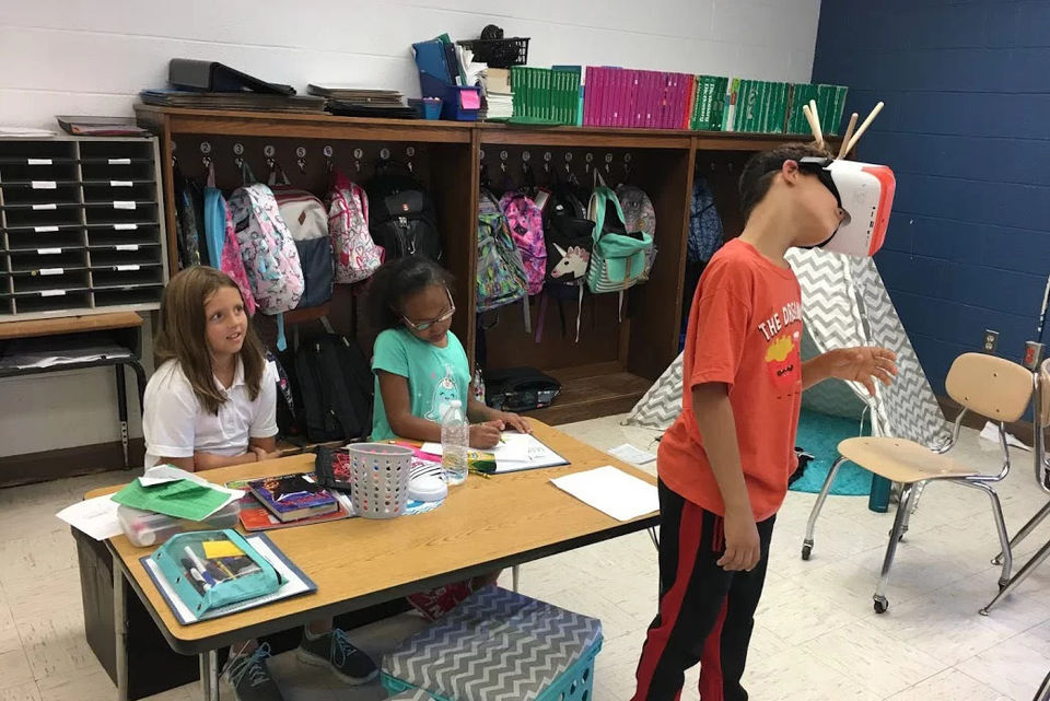 One student wearing a VR headset while two others watch, engaging in immersive classroom learning.