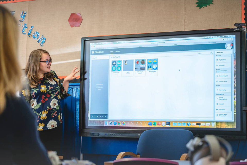 Teacher stood in front of a classroom panel looking at the ClassVR portal with their class