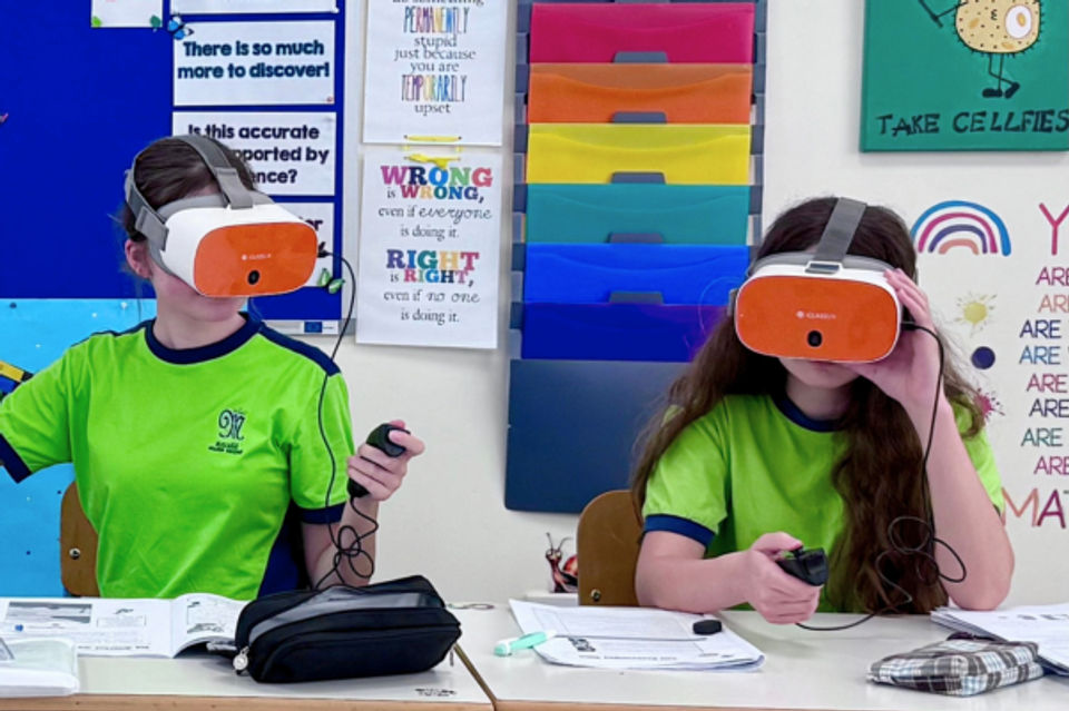 Two students sat at their desk, wearing VR headsets and using controllers
