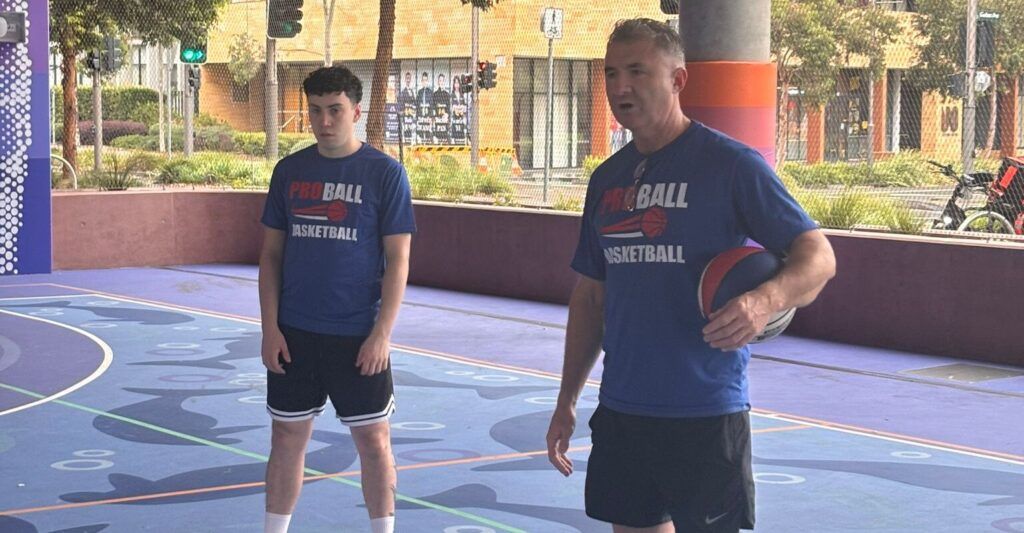 Coach guiding young children during a MiniBall basketball session while players practice beginner skills on the court.