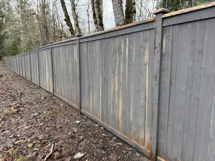Failed fence stain with peeling and dark blotches from moisture entrapment