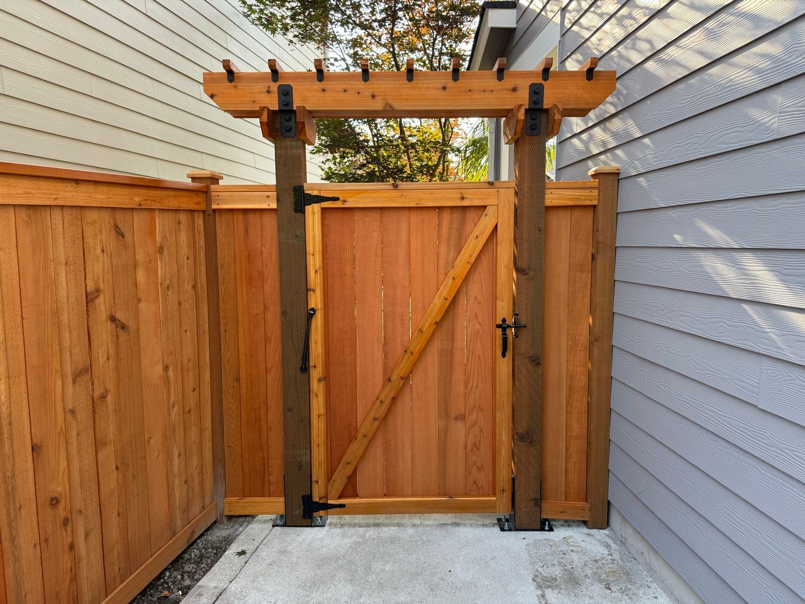 Cedar gate with pergola arbor top between two houses, decorative brackets and finials, black metal hardware