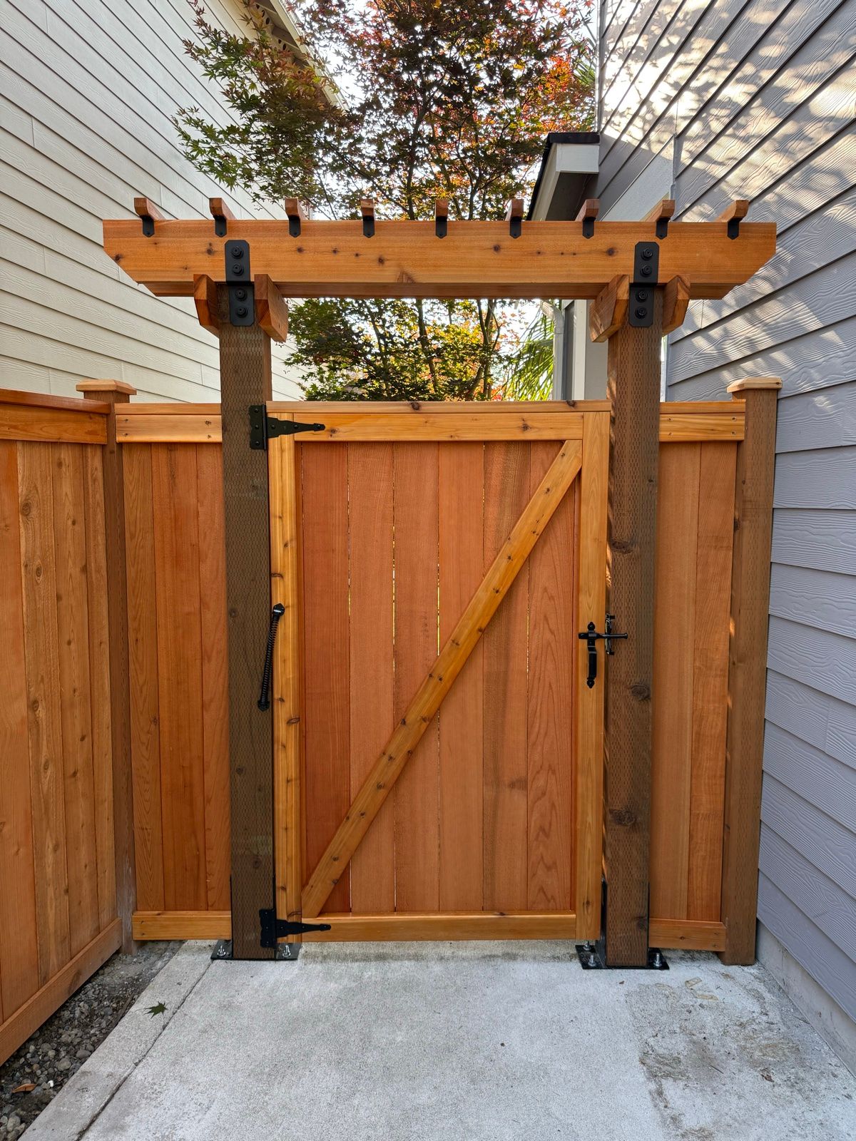 Gate mounted on concrete walkway with trellis above, concrete brackets securing posts, self-closing spring attached