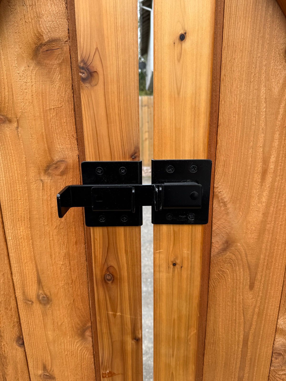 Close-up of gravity-style drop-bolt latch mounted across horizontal cedar planks, black metal mechanism