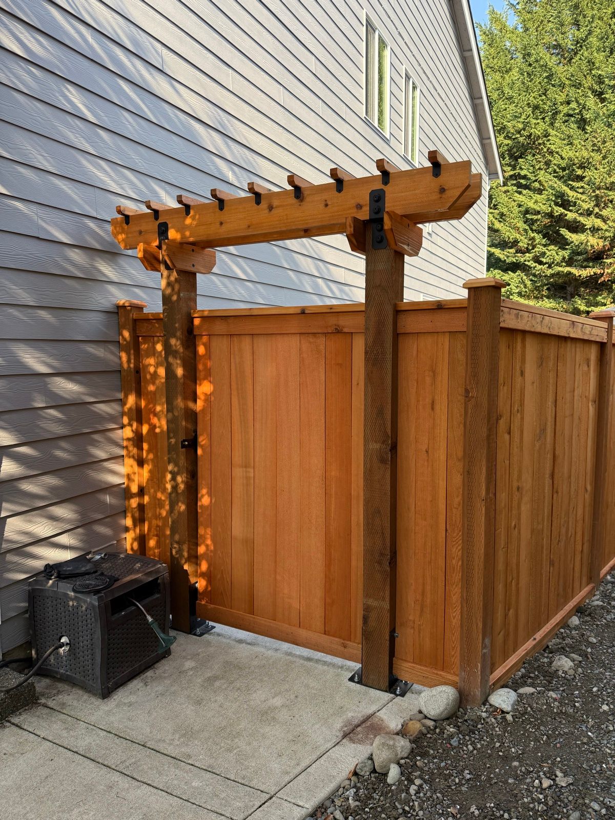 Privacy fence with decorative trellis on corner post, horizontal cedar planks, grey house siding in background