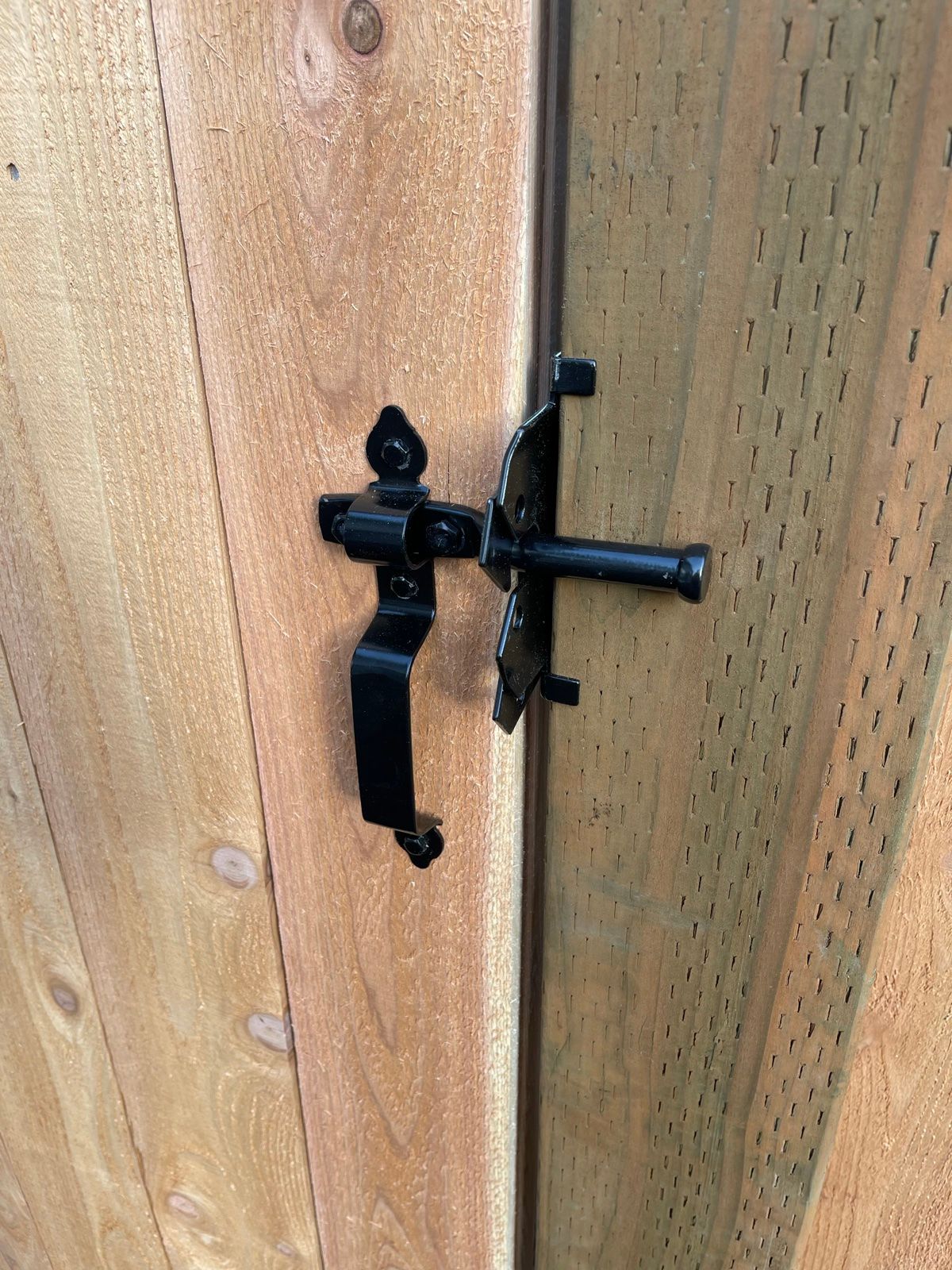 Close-up of sliding barrel bolt latch mounted on horizontal cedar planks, black metal with scrolled base plate
