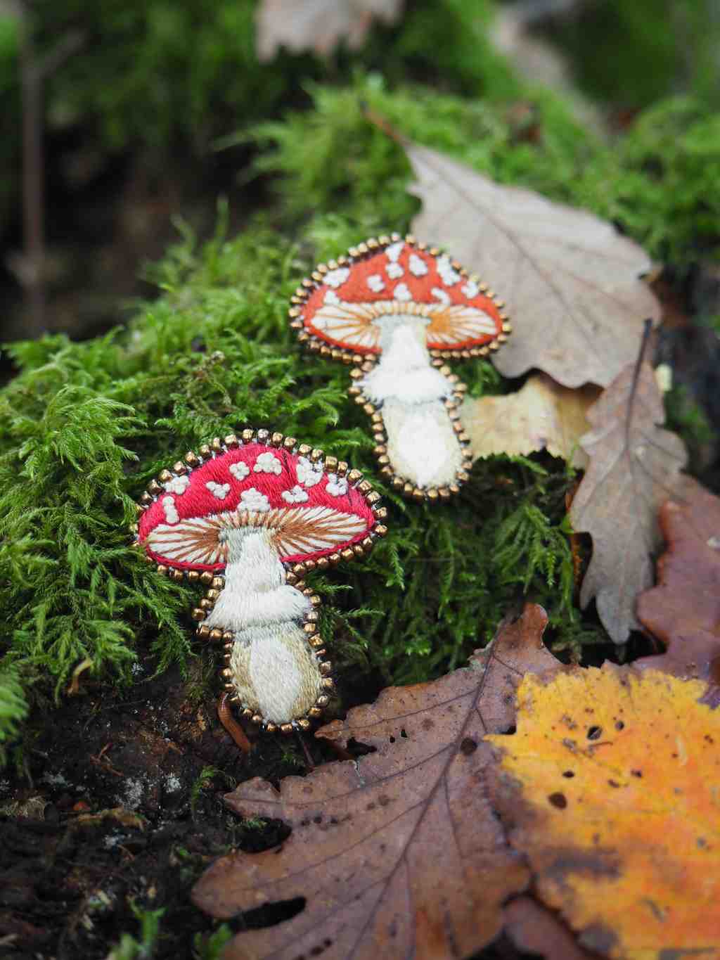 Cette image présente une scène forestière enchantée avec deux champignons décoratifs aux couleurs vives posés sur un tronc d'arbre recouvert de mousse.  **Éléments principaux :**
- **Champignons** : Deux champignons artificiels ou stylisés avec des chapeaux rouge vif ornés de points blancs caractéristiques, rappelant les amanites tue-mouches. Ils ont des pieds blancs et semblent être des objets décoratifs plutôt que de vrais champignons. **Environnement :**
- **Support** : Un tronc d'arbre ou une branche recouverte d'une mousse verte luxuriante et dense
- **Feuillage** : Des feuilles d'automne aux teintes dorées et orangées parsèment la scène
- **Arrière-plan** : Végétation floue créant une atmosphère forestière naturelle **Ambiance :**
L'image évoque un conte de fées ou un univers fantastique, avec ses couleurs contrastées - le rouge éclatant des champignons contre le vert intense de la mousse. La composition crée une atmosphère magique et féerique, typique des illustrations de contes pour enfants. La profondeur de champ met l'accent sur les champignons décoratifs tout en conservant le contexte naturel de la forêt.