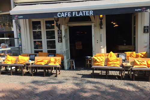 Café Flater storefront with yellow cushioned outdoor seating and dark interior visible through windows, ready for live music performances.