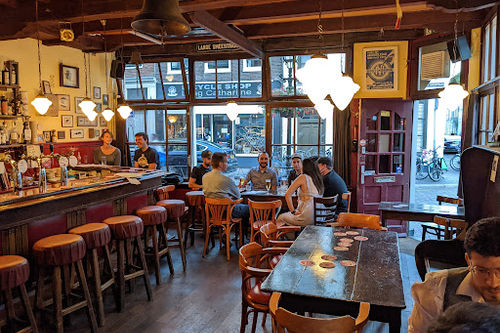 Café DeRat interior with bar seating, wooden beams, stage lighting, and audience seating arranged for live music performances.