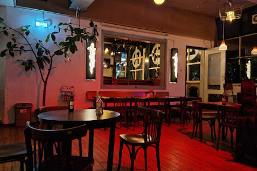 dB's oefenstudio's concert hall with red-lit interior, black tables and chairs, stage area with professional lighting and PA system for live music performances.