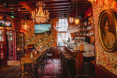 Tante Cor intimate live music bar with ornate decor, chandeliers, wooden beams, and vintage portraits creating warm performance atmosphere.